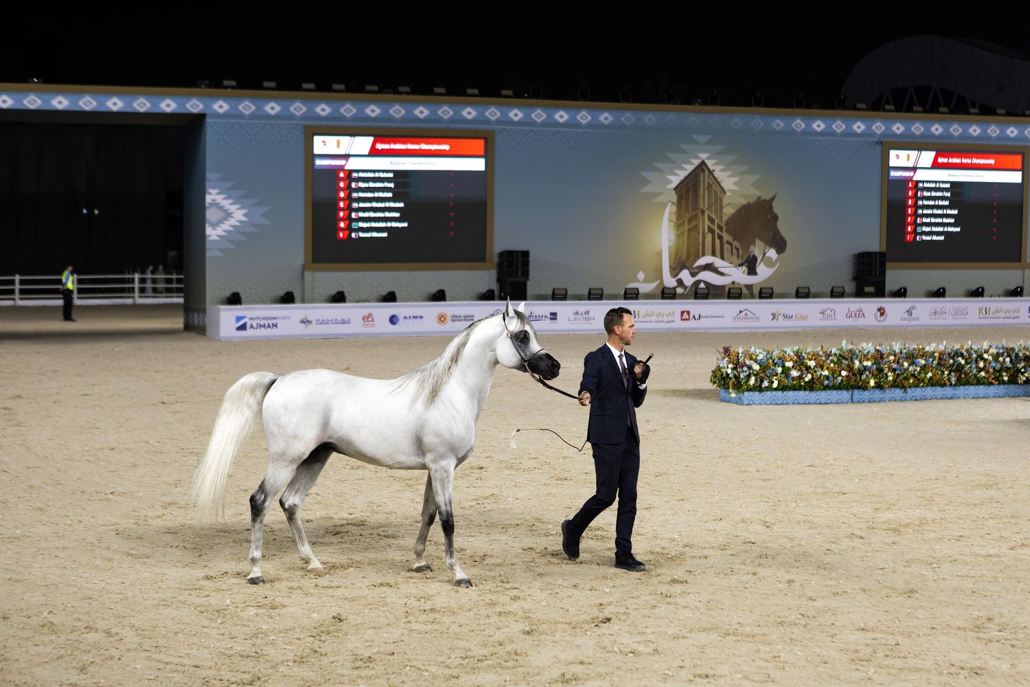 White horses perform in an indoor arena during an equestrian demonstration.