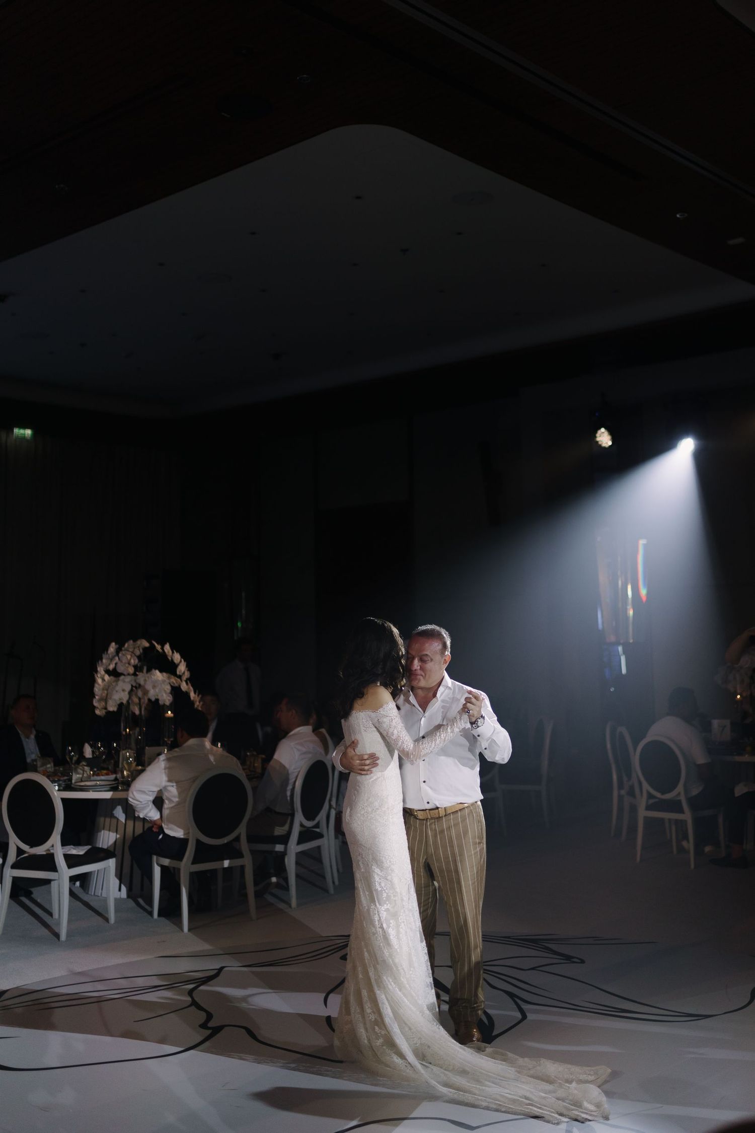 Dimly lit ballroom with elegant white chairs and dramatic spotlighting.
