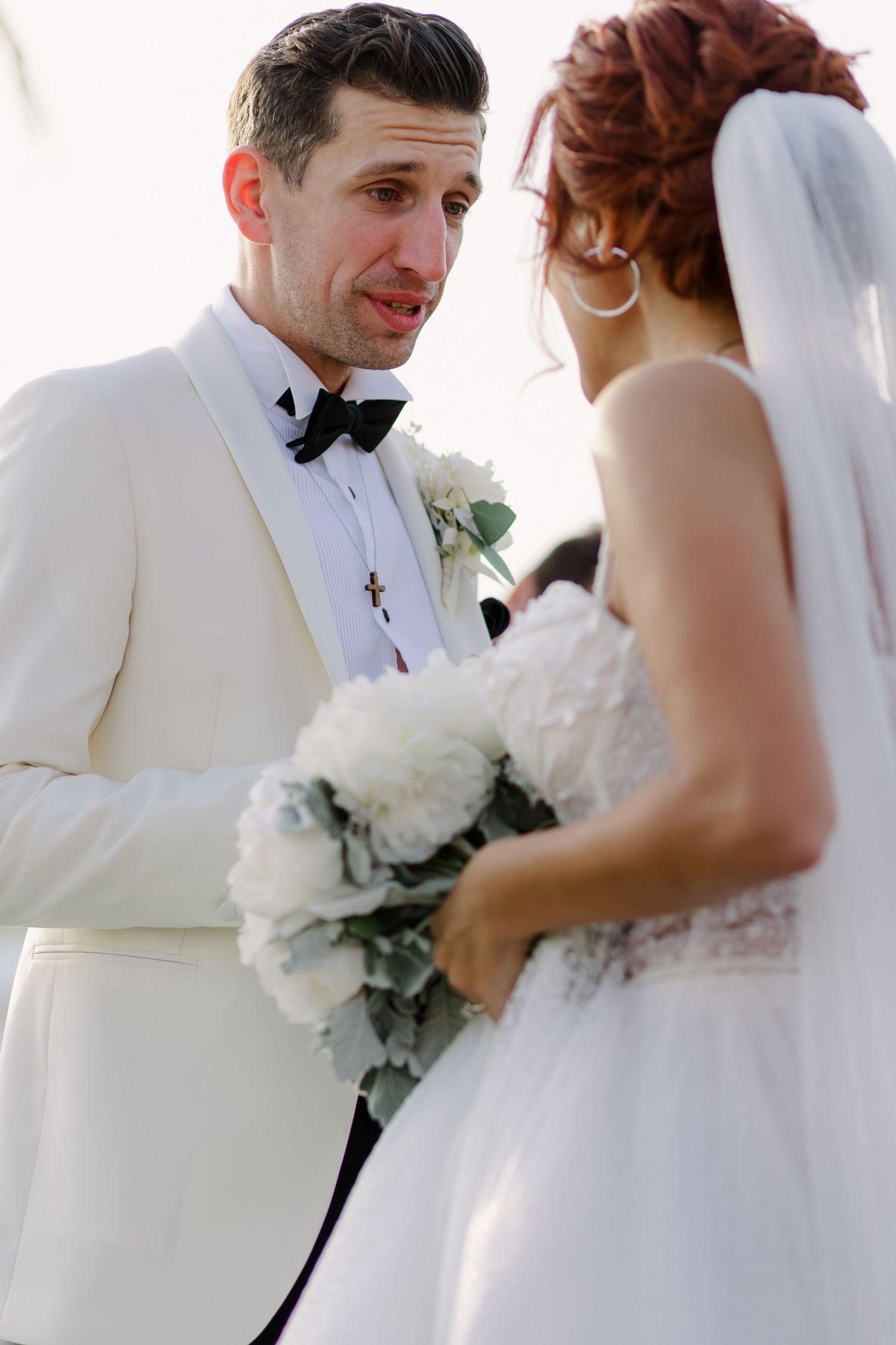 Couple in white formal attire exchanging flowers during wedding ceremony.