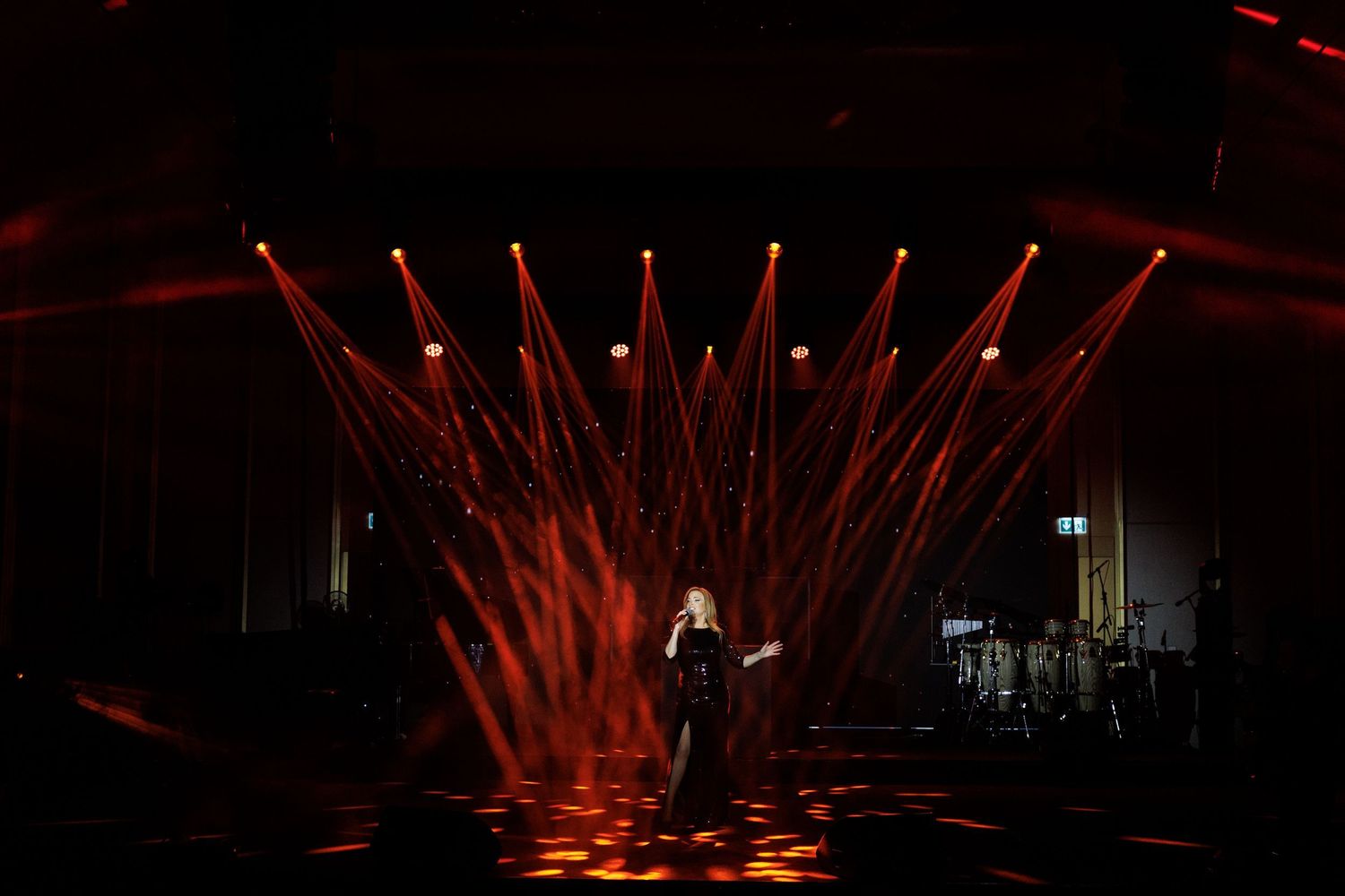 Red concert lighting creates geometric patterns of beams across a dark stage.