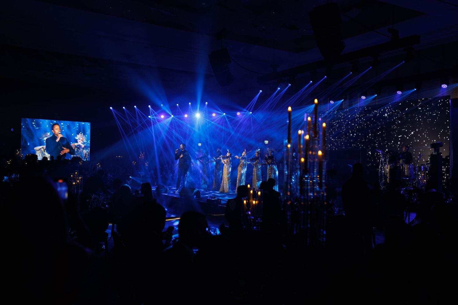 Concert venue illuminated with blue lights and a large crowd visible in silhouette.
