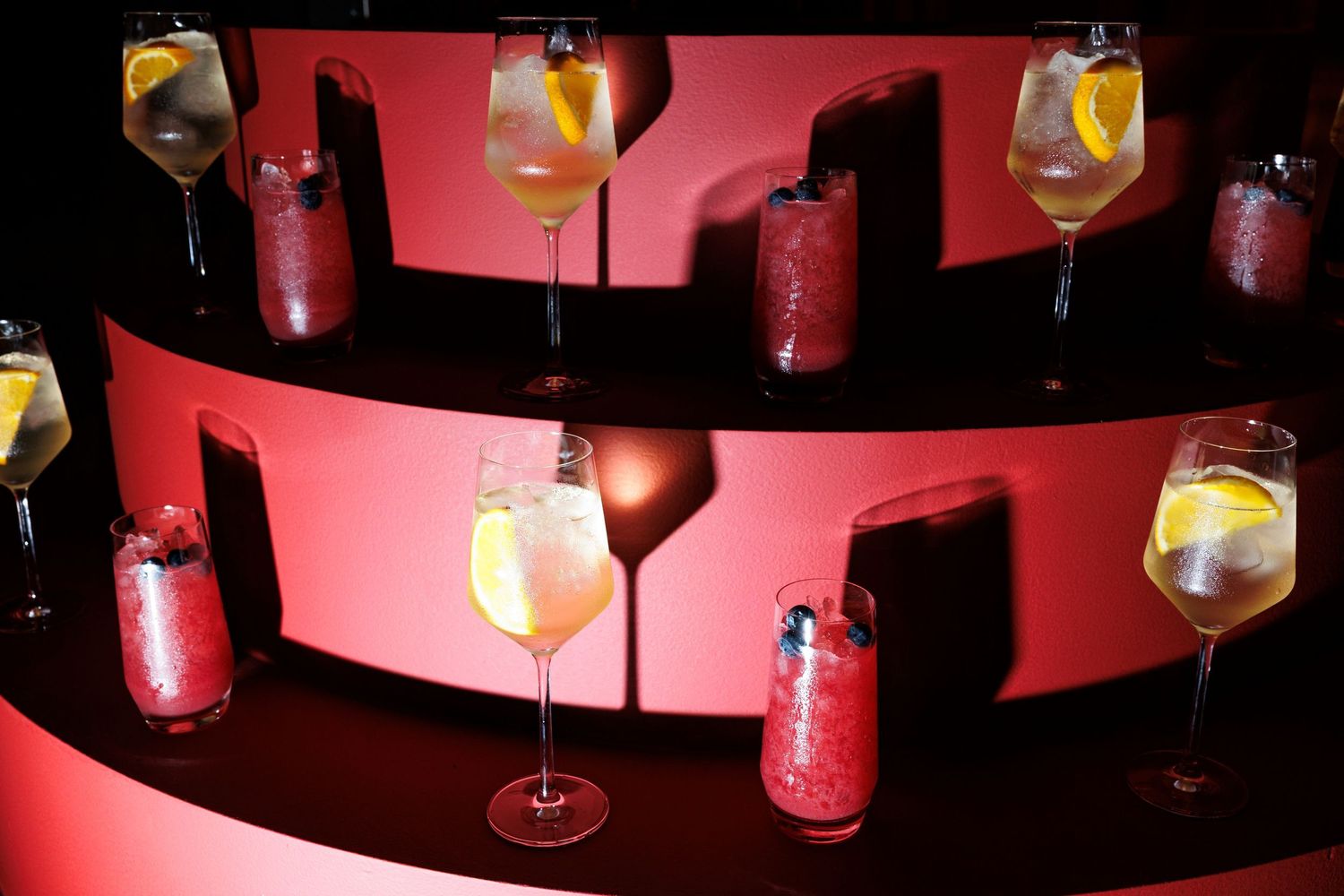 Elegant cocktails with citrus garnishes displayed on a bar with dramatic red lighting.
