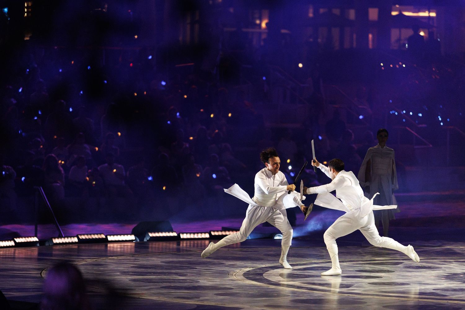 Performers in white costumes glide gracefully across a dark ice rink during an evening show.