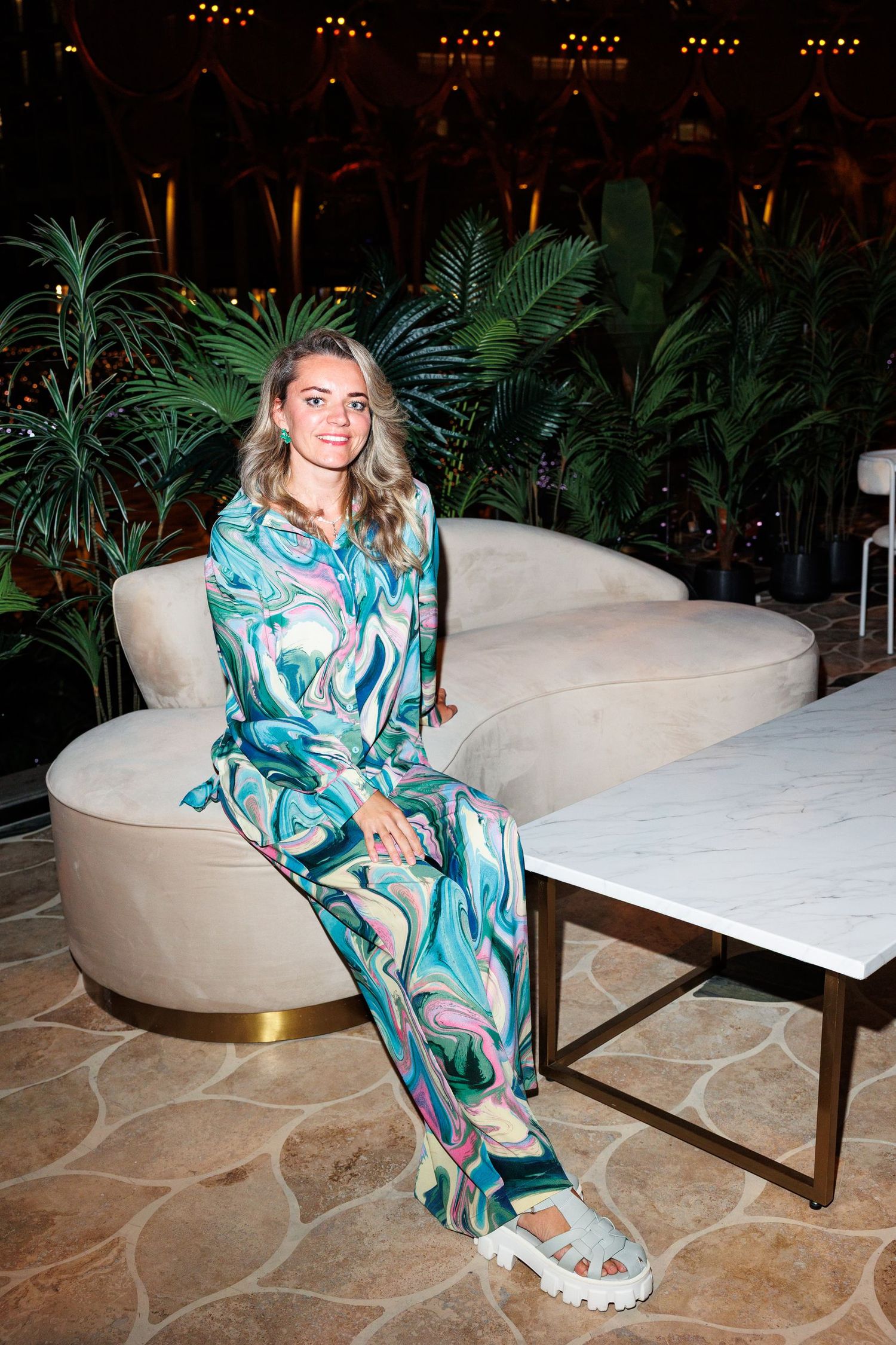 Person in tropical print dress lounges on white modern furniture at evening event.
