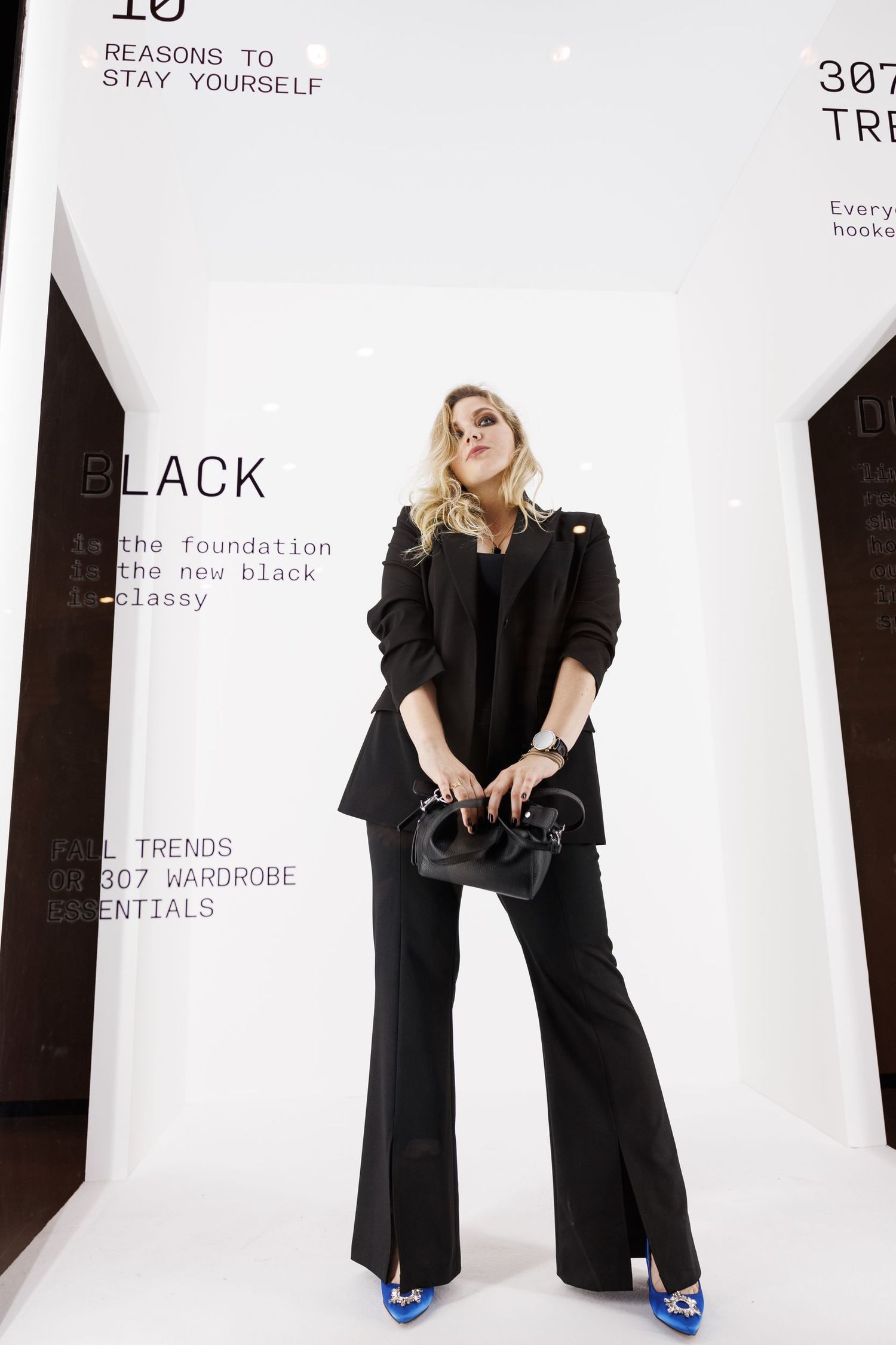 Model wearing all black ensemble with bright blue shoes in studio setting.