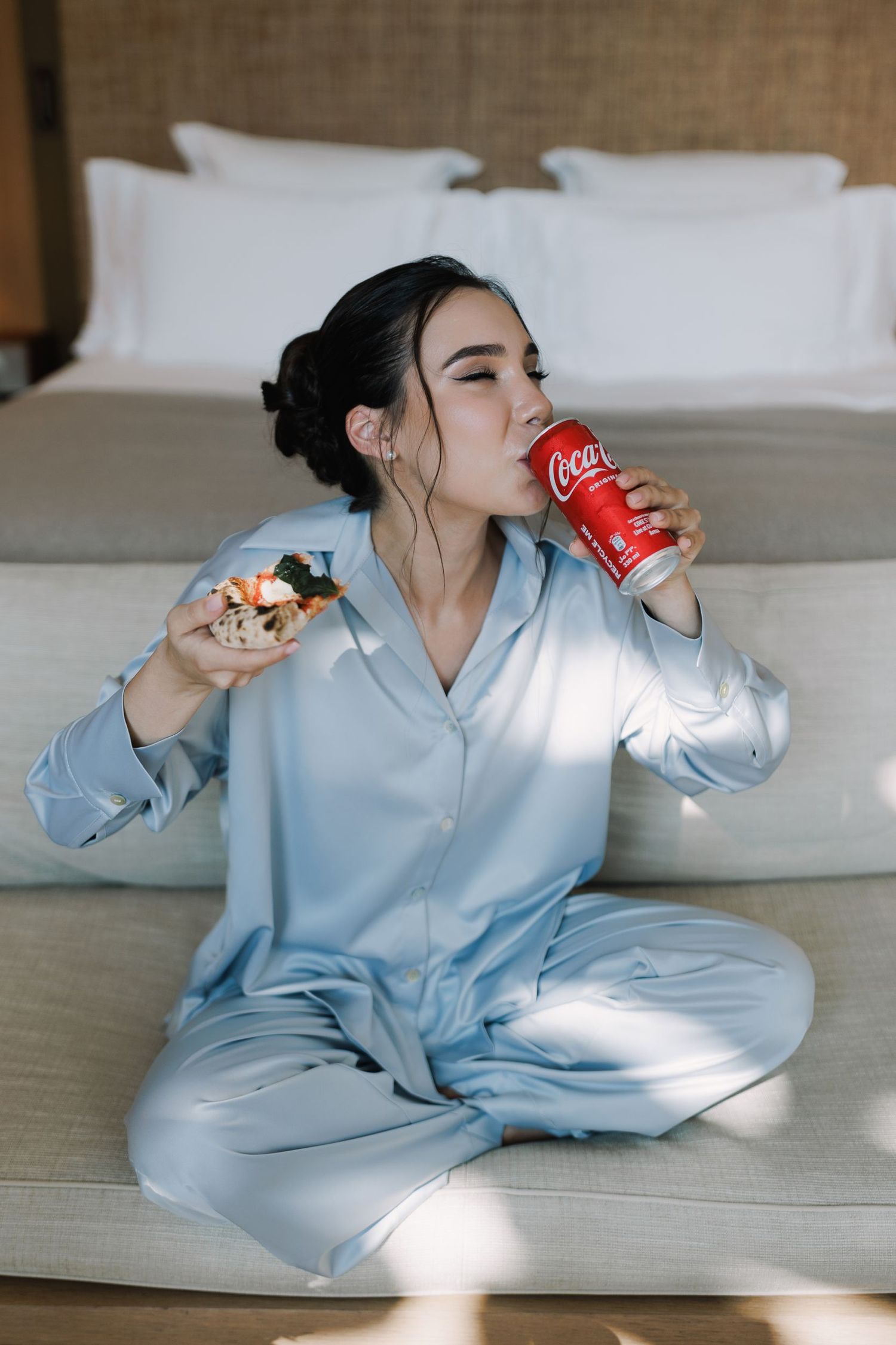 Person in blue pajamas enjoying pizza and Coca-Cola on a couch.