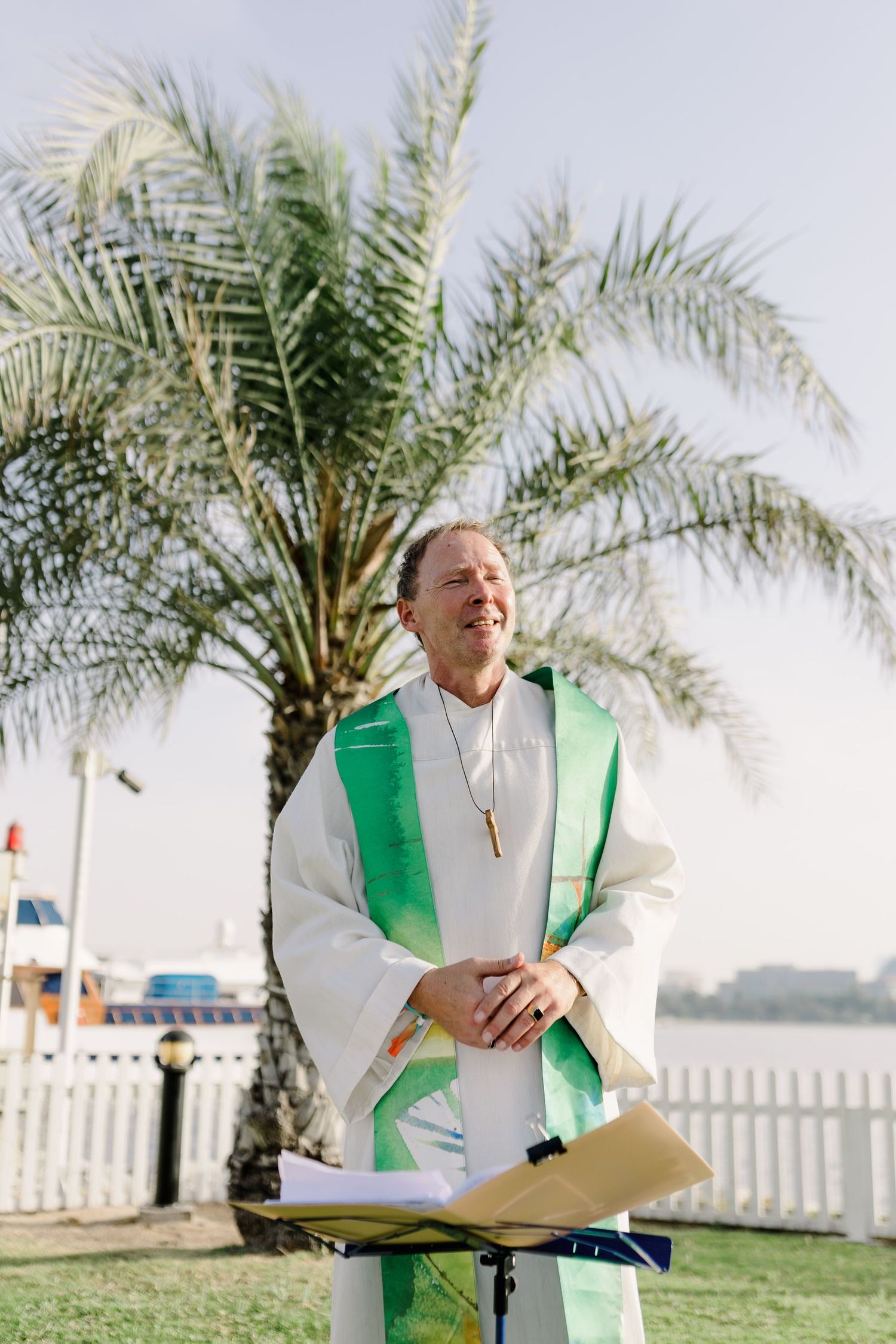 Wedding officiant in white robes with green stole preparing for outdoor ceremony.