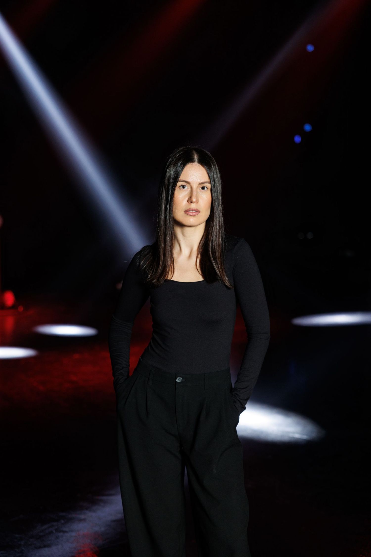 Model walking runway in black outfit under dramatic stage lighting.