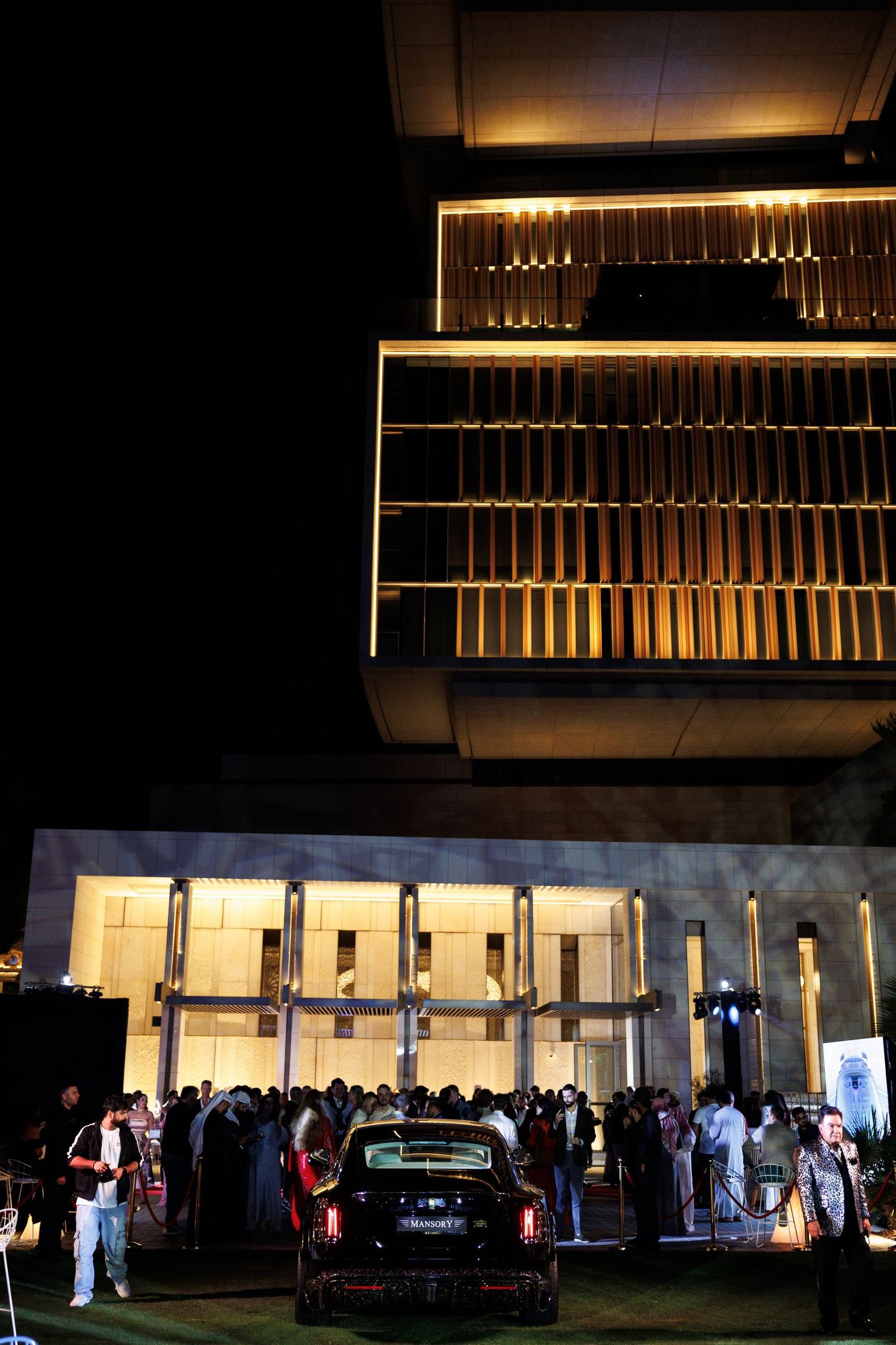 Nighttime event gathering outside a building with illuminated gold panels.