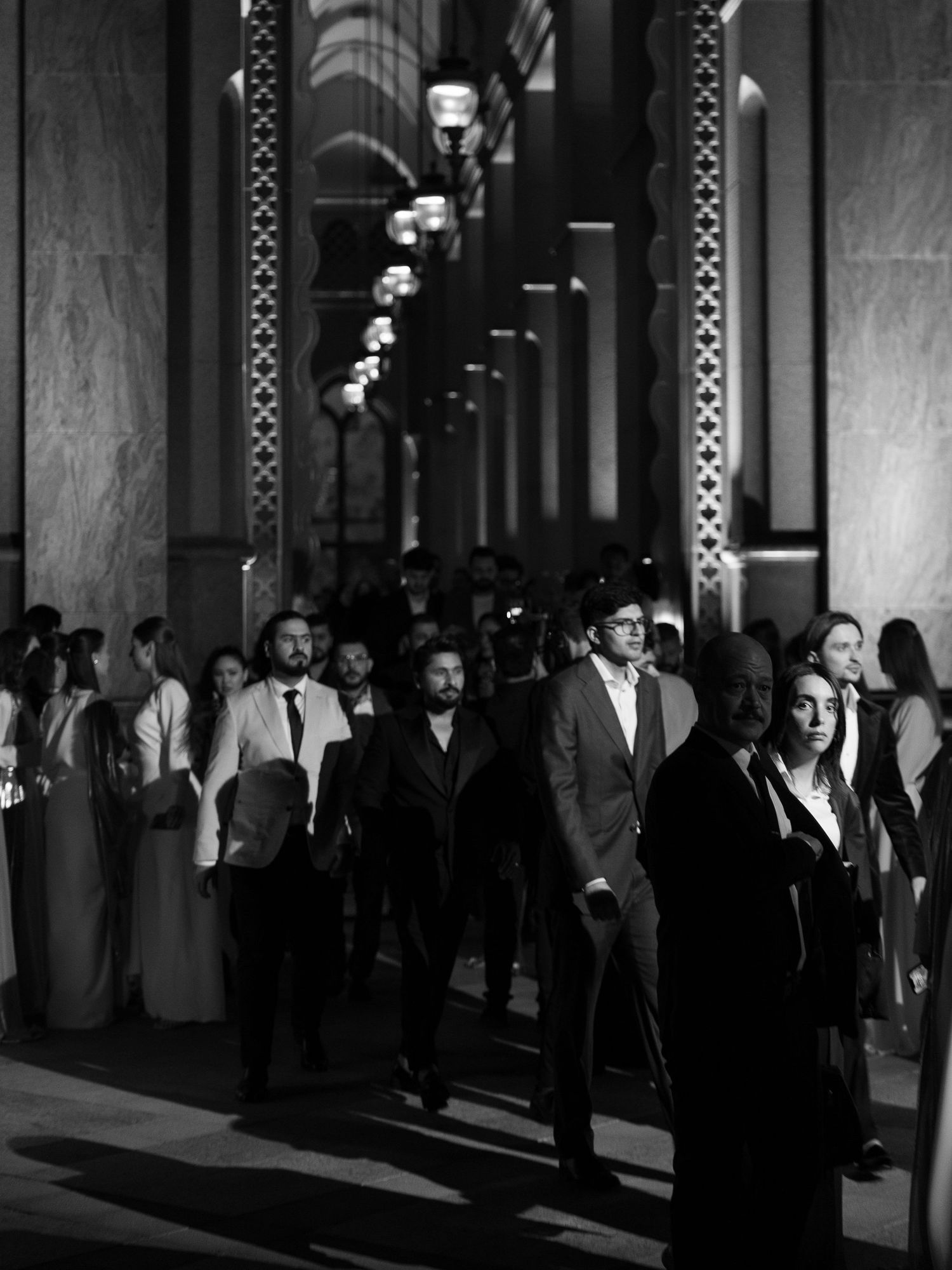 A black and white photograph showing a crowded corridor with dramatic lighting and shadows.