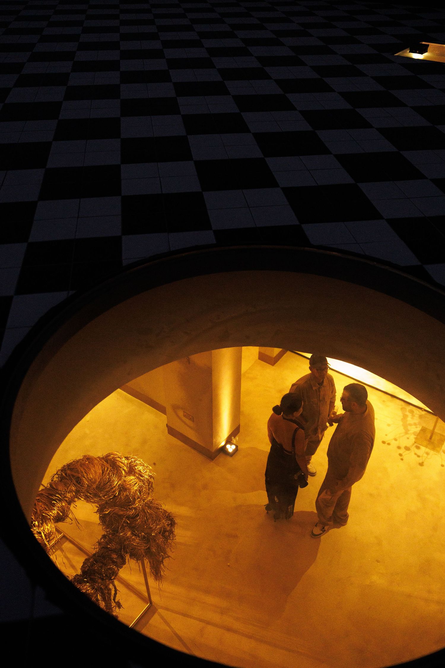 Checkered floor with shadows and figures illuminated by warm lighting from below.