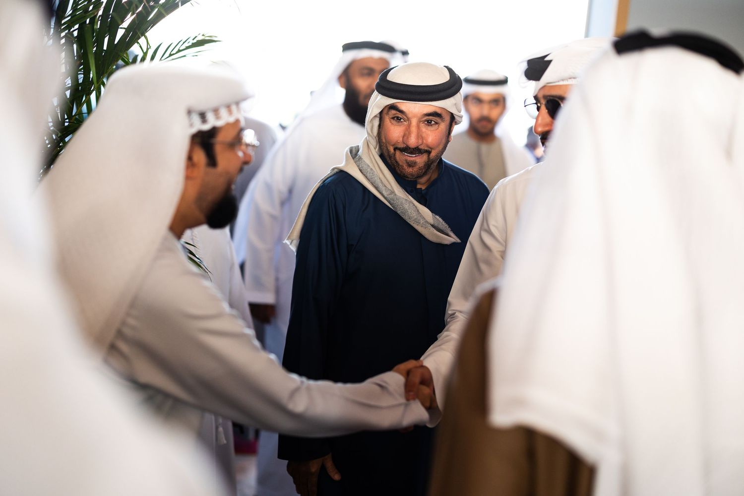 Traditional Emirati gathering shows men in white kanduras greeting each other at a cultural event.