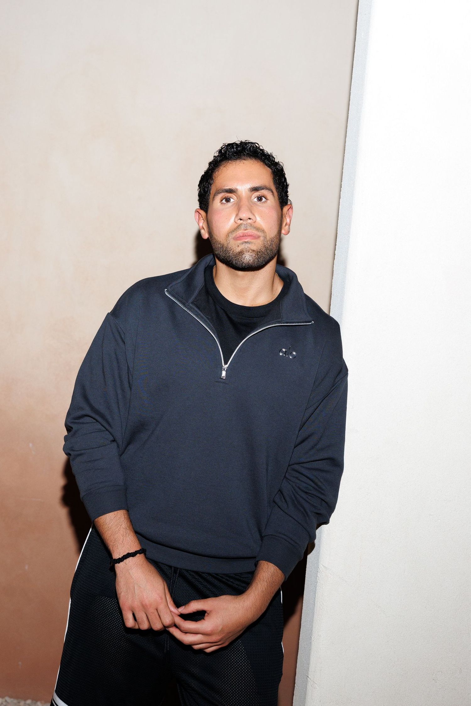 Person in dark casual attire posing against light colored wall.