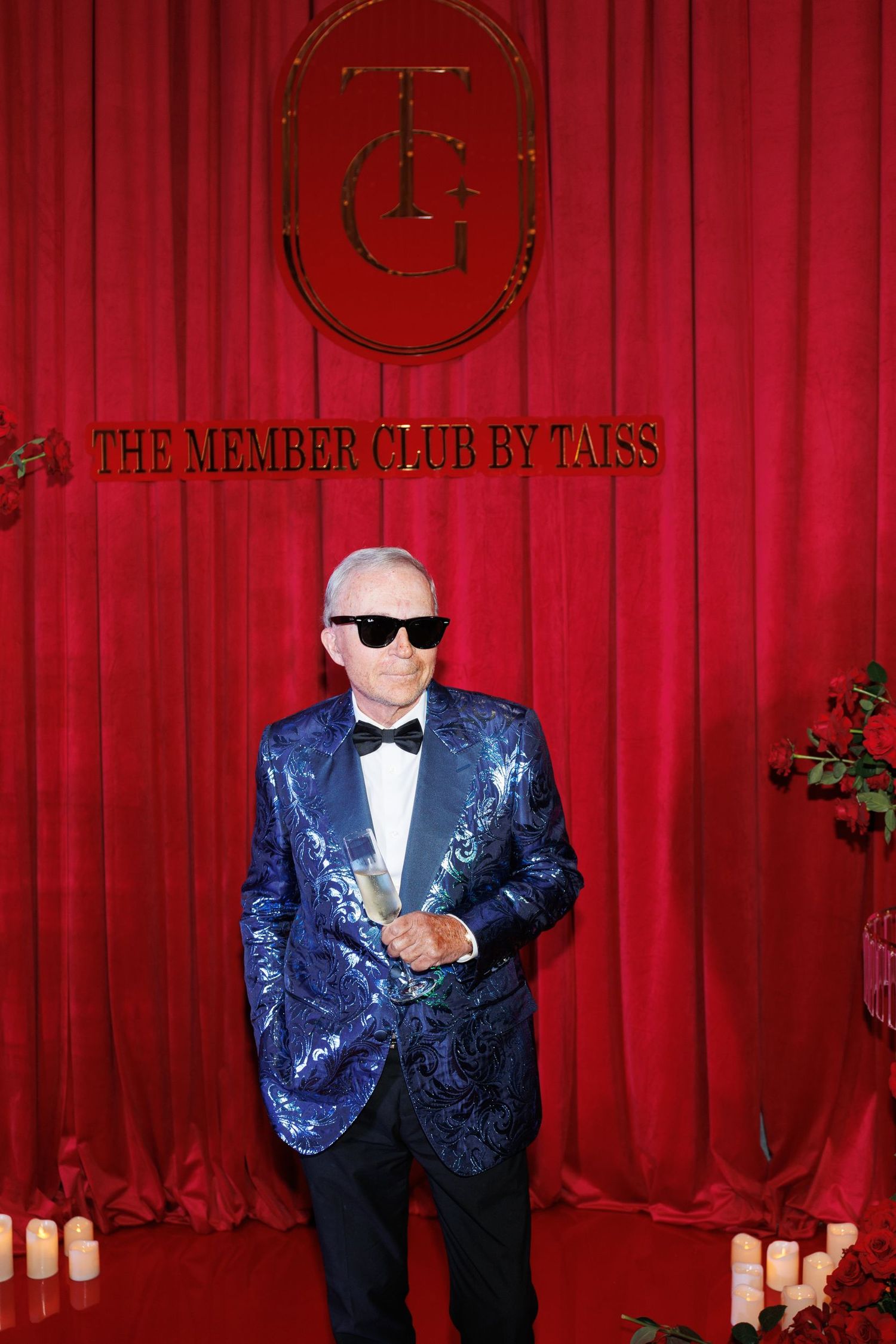 Guest wearing blue sequined tuxedo jacket and sunglasses at formal red carpet event.