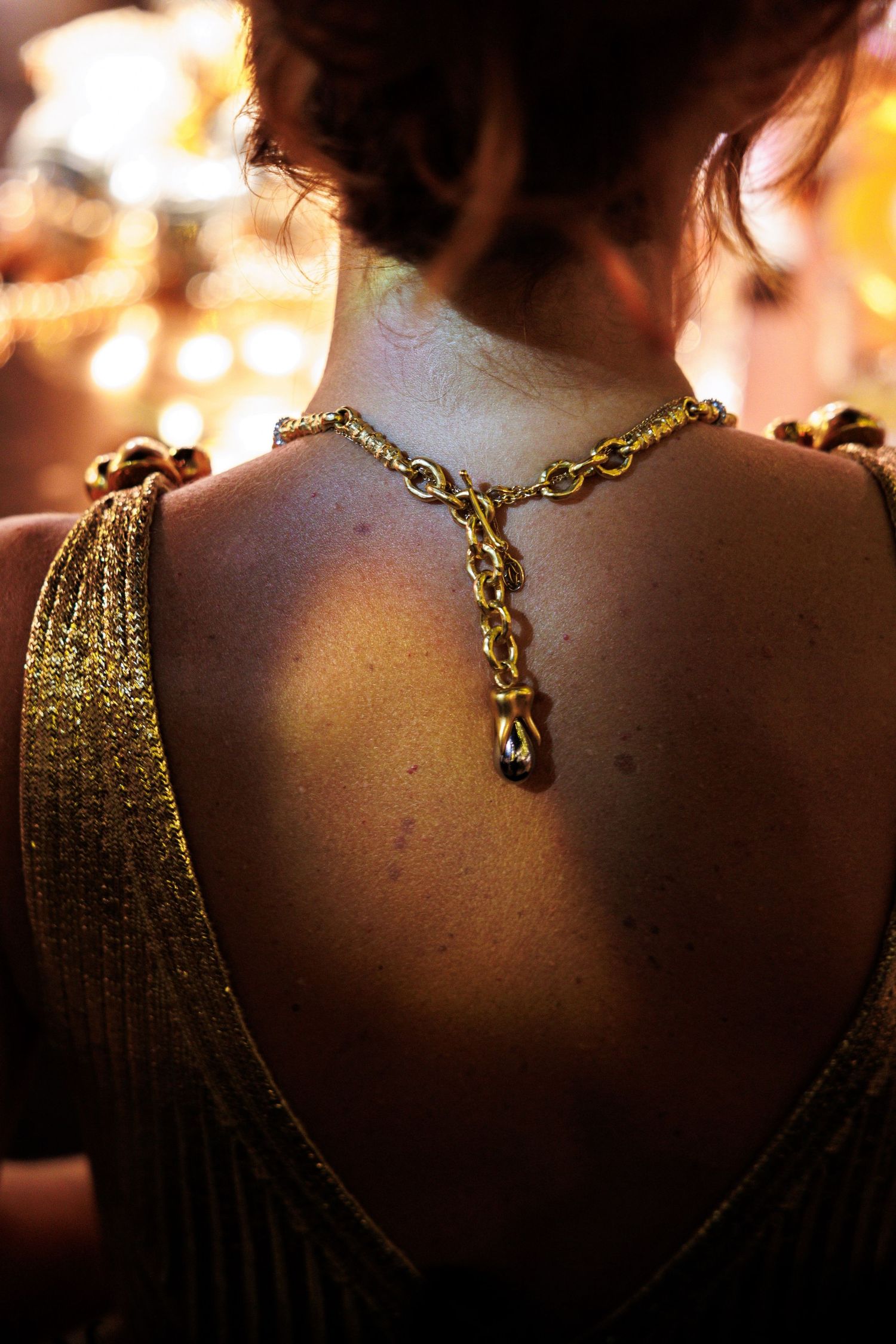 Close-up of a gold chain necklace against dark skin in warm lighting.