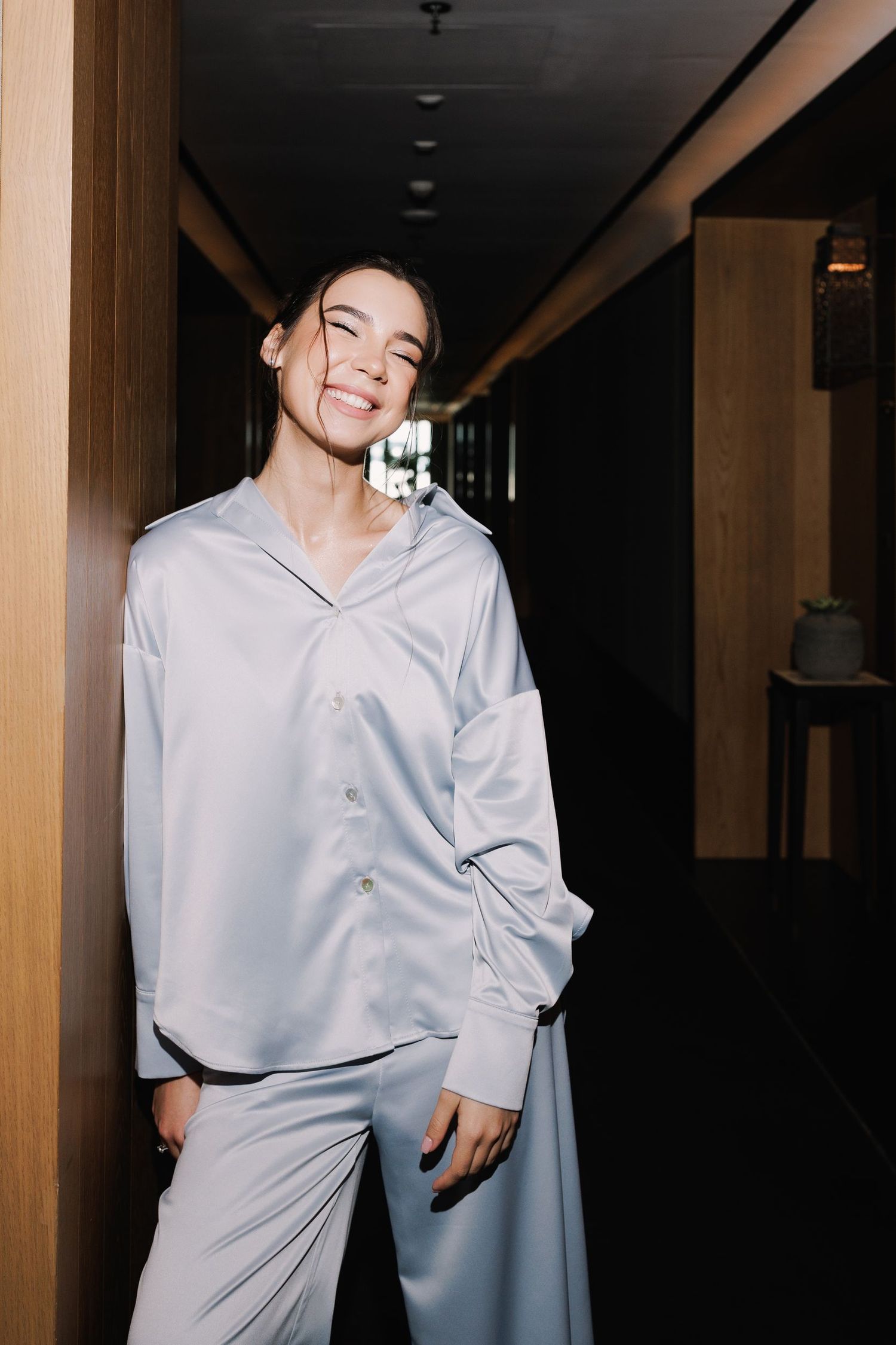 Candid fashion portrait in hotel corridor wearing relaxed light-colored ensemble.