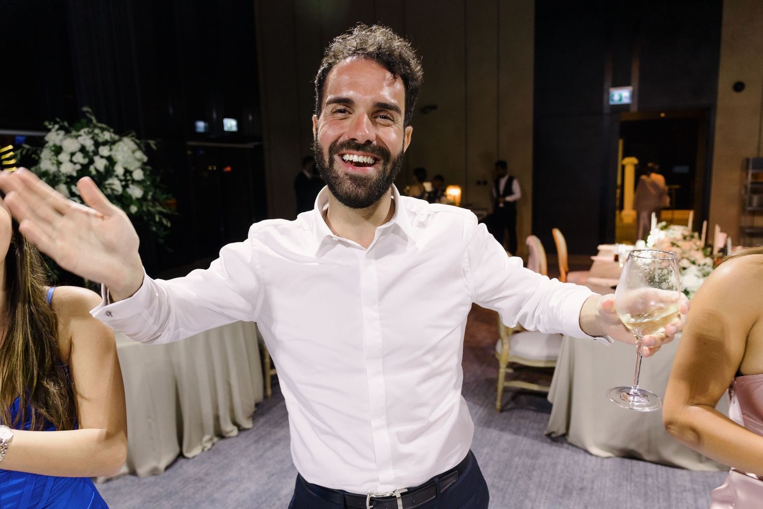 A joyful guest celebrates at a wedding reception with arms outstretched in a white dress shirt.