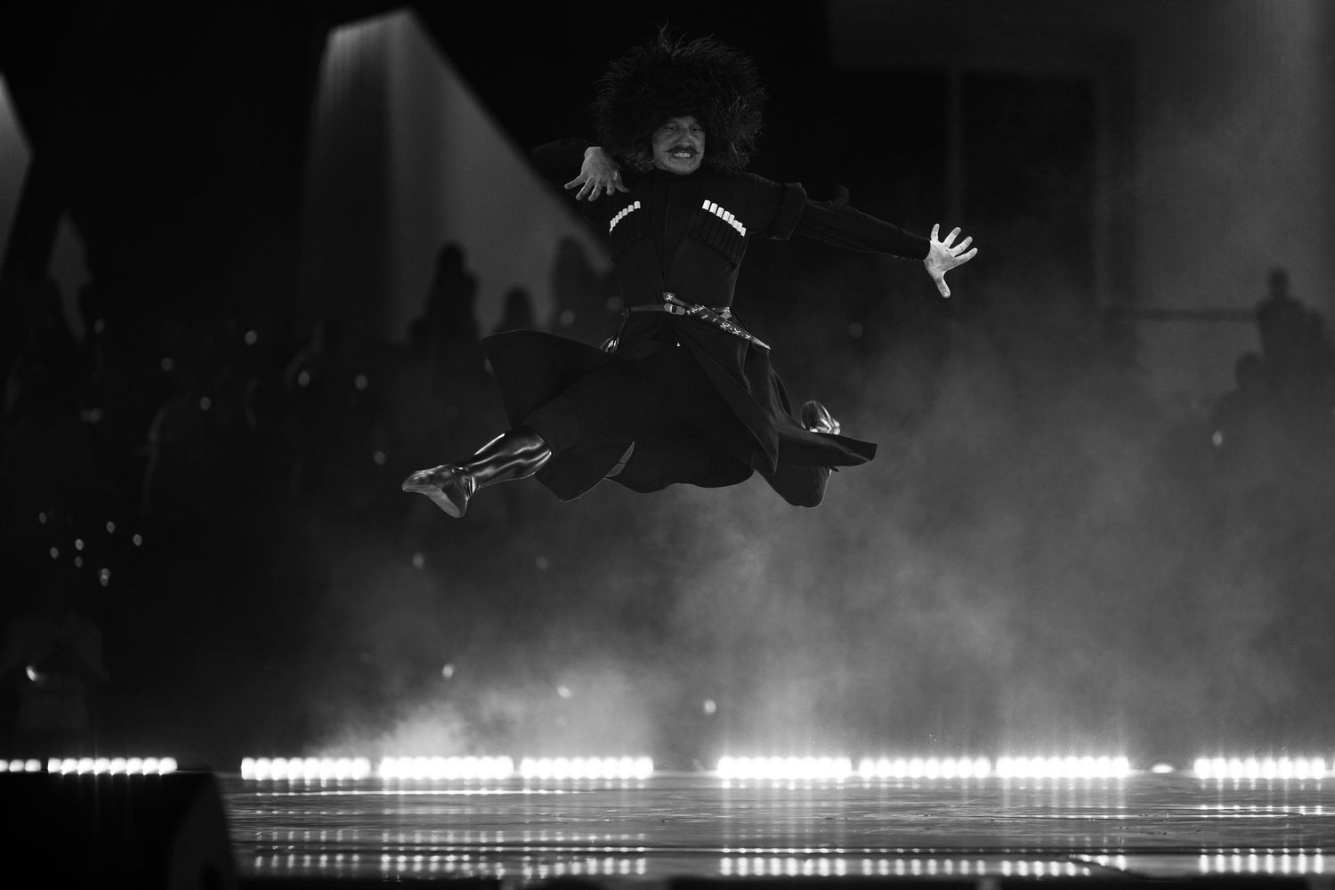 Black and white performance shot capturing dynamic movement across a dimly lit stage.