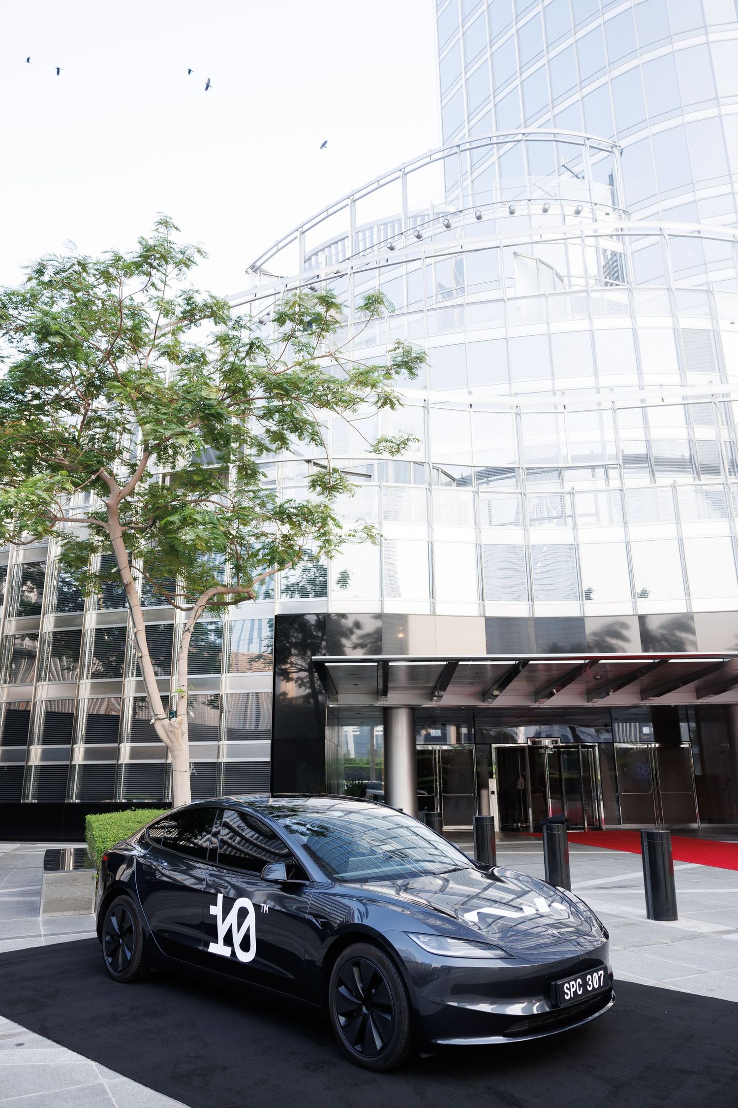 Modern glass building exterior with black luxury cars parked in front.
