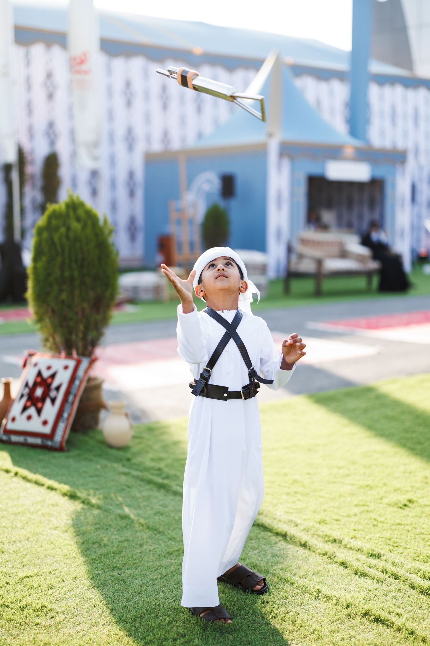 A person in white traditional Middle Eastern clothing performs a sequence of movements on grass near a blue building.