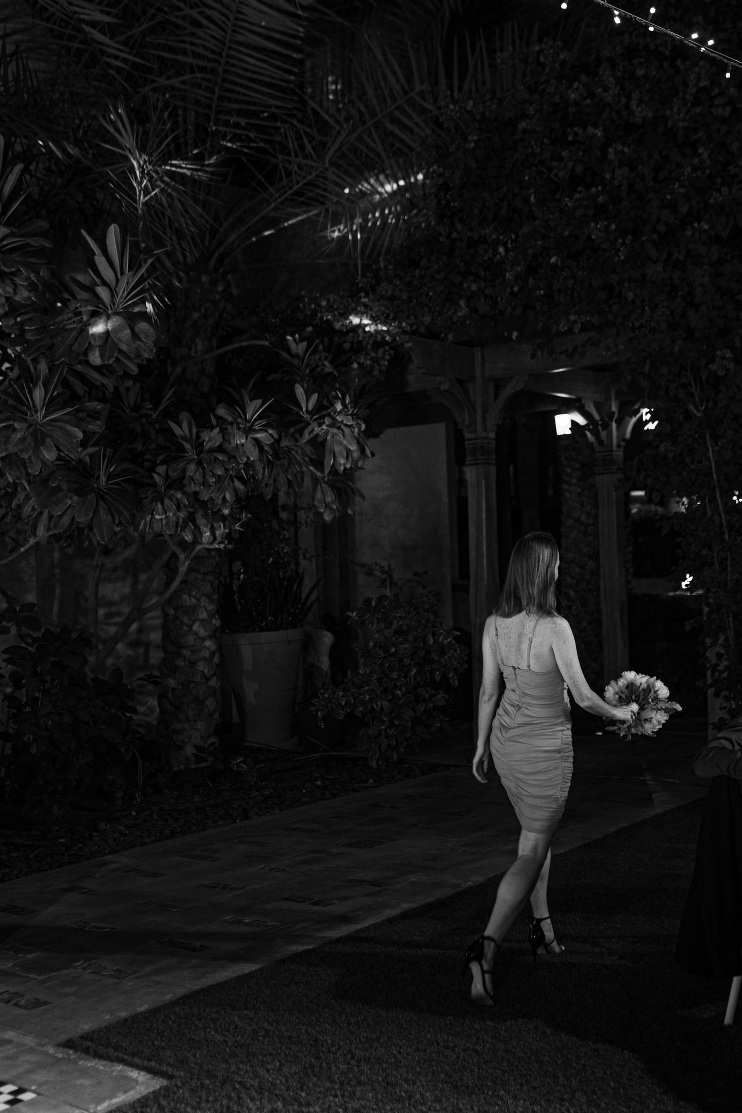 Guests walk through dimly lit outdoor garden pathway during evening event.