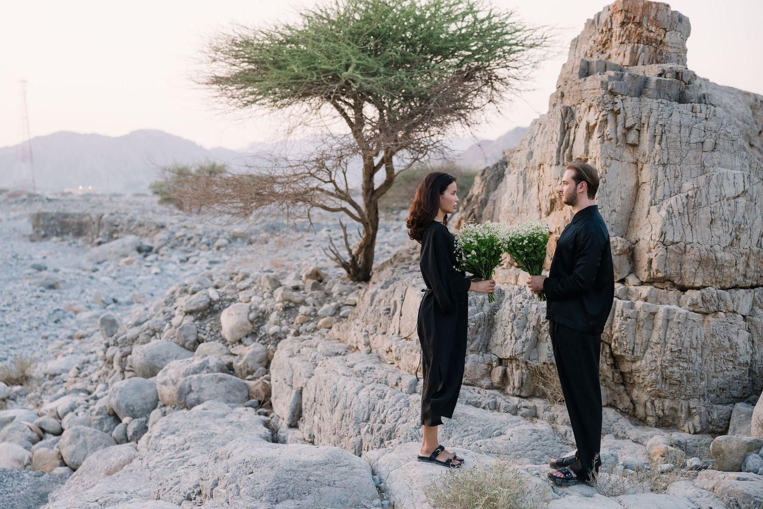 Desert wedding photo session among rocky terrain and sparse acacia trees.