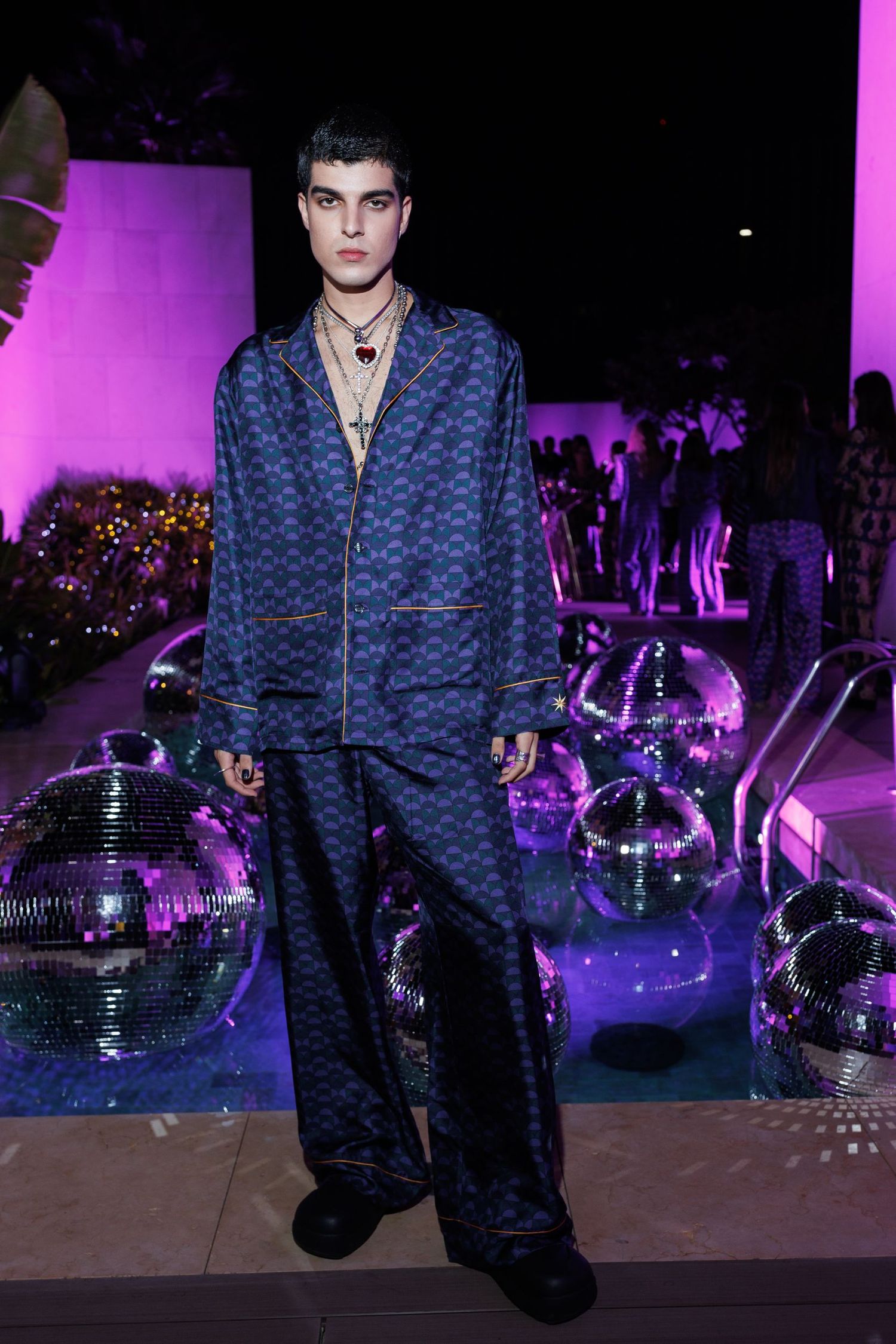Model in dark patterned outfit poses dramatically with disco balls under purple lighting.