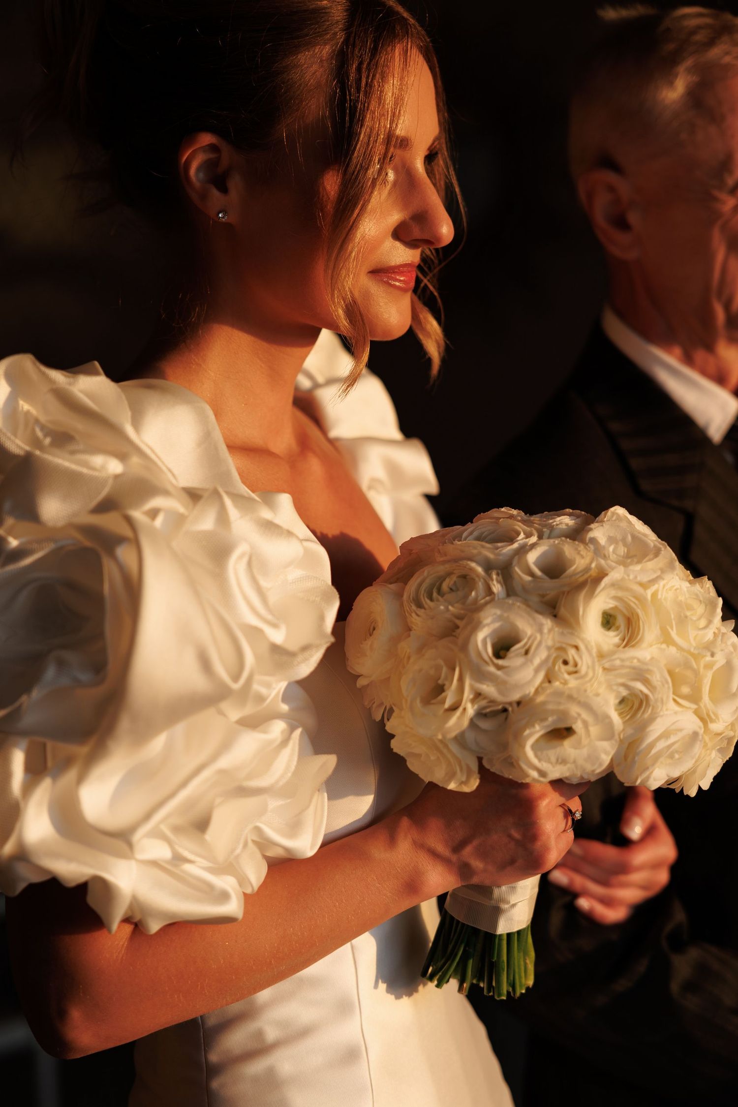 Artistic wedding photo focusing on white rose bouquet in dramatic lighting.