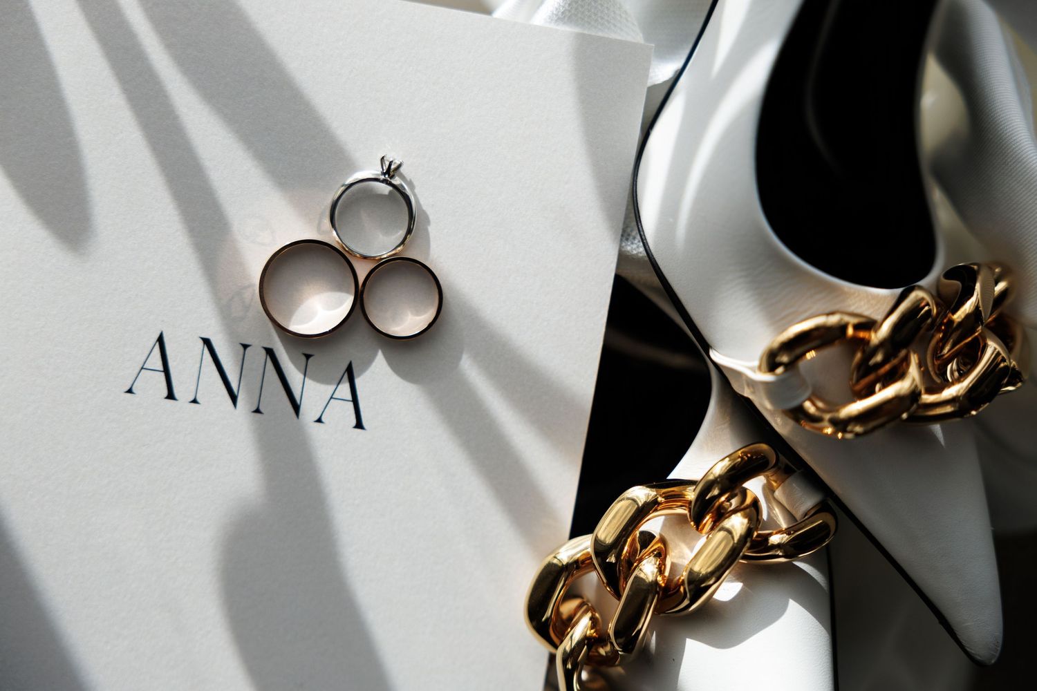 Wedding rings and jewelry artistically arranged on white surface with shadows.