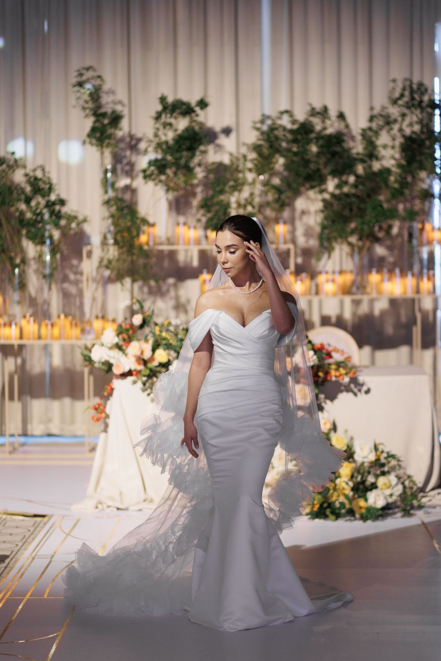 Elegant white wedding dress flowing across a modern event space with decorative greenery and warm lighting.