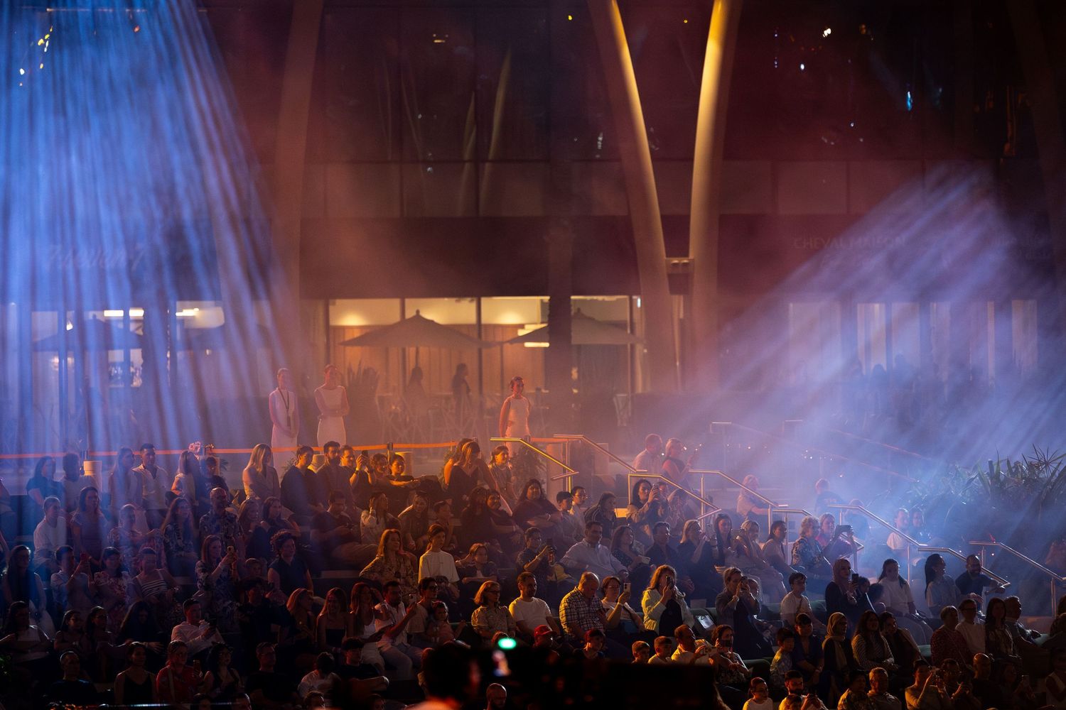 Crowd at a concert venue with dramatic blue spotlights and fog effects creating atmosphere.