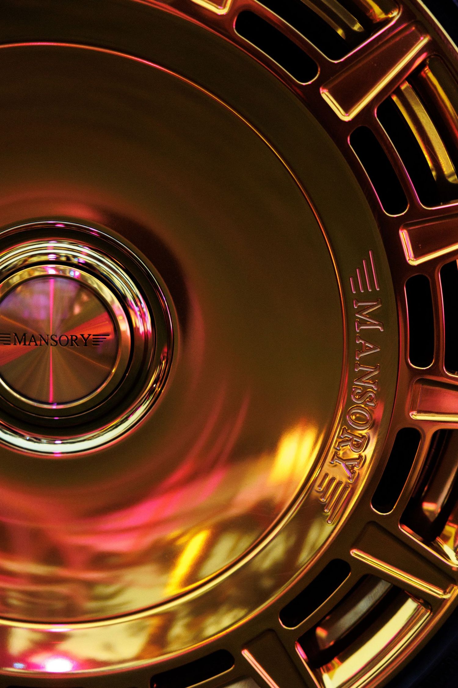 Luxury car wheel rim detail with metallic finish reflecting red and gold lighting.