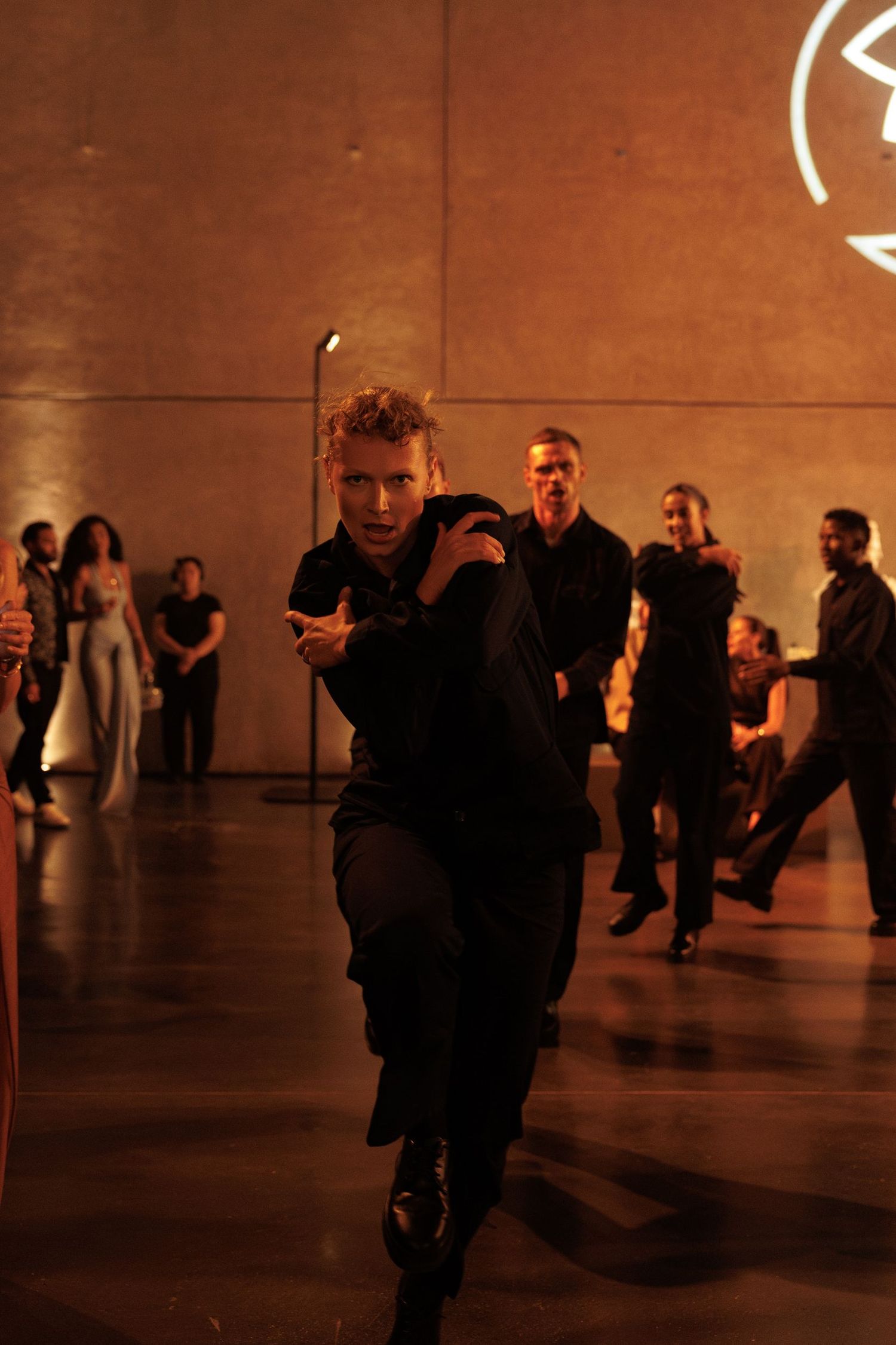 People gather in a dimly lit indoor space with warm amber lighting and reflective surfaces.