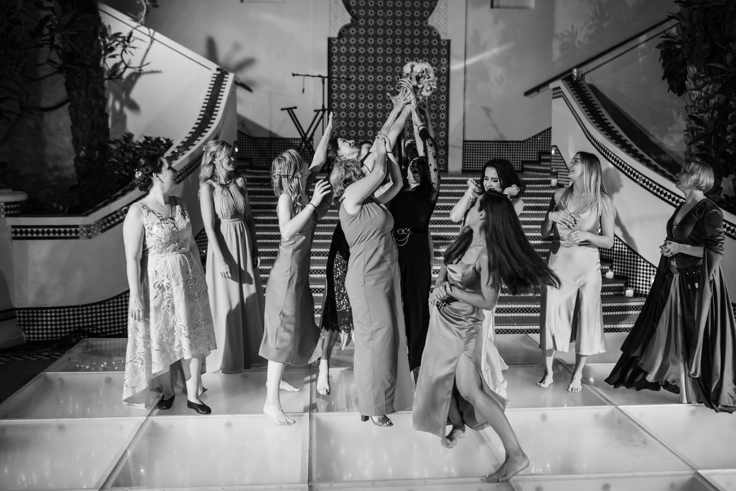 Group performs synchronized dance moves at wedding reception in black and white.