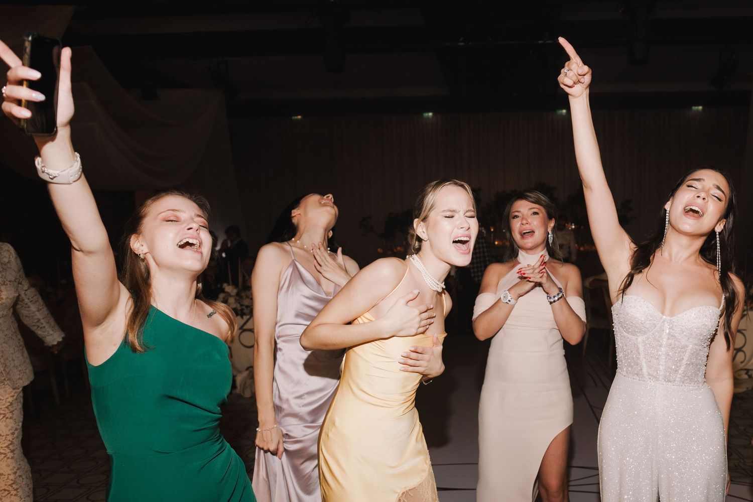 Wedding party guests dancing and celebrating with raised arms on the dance floor.