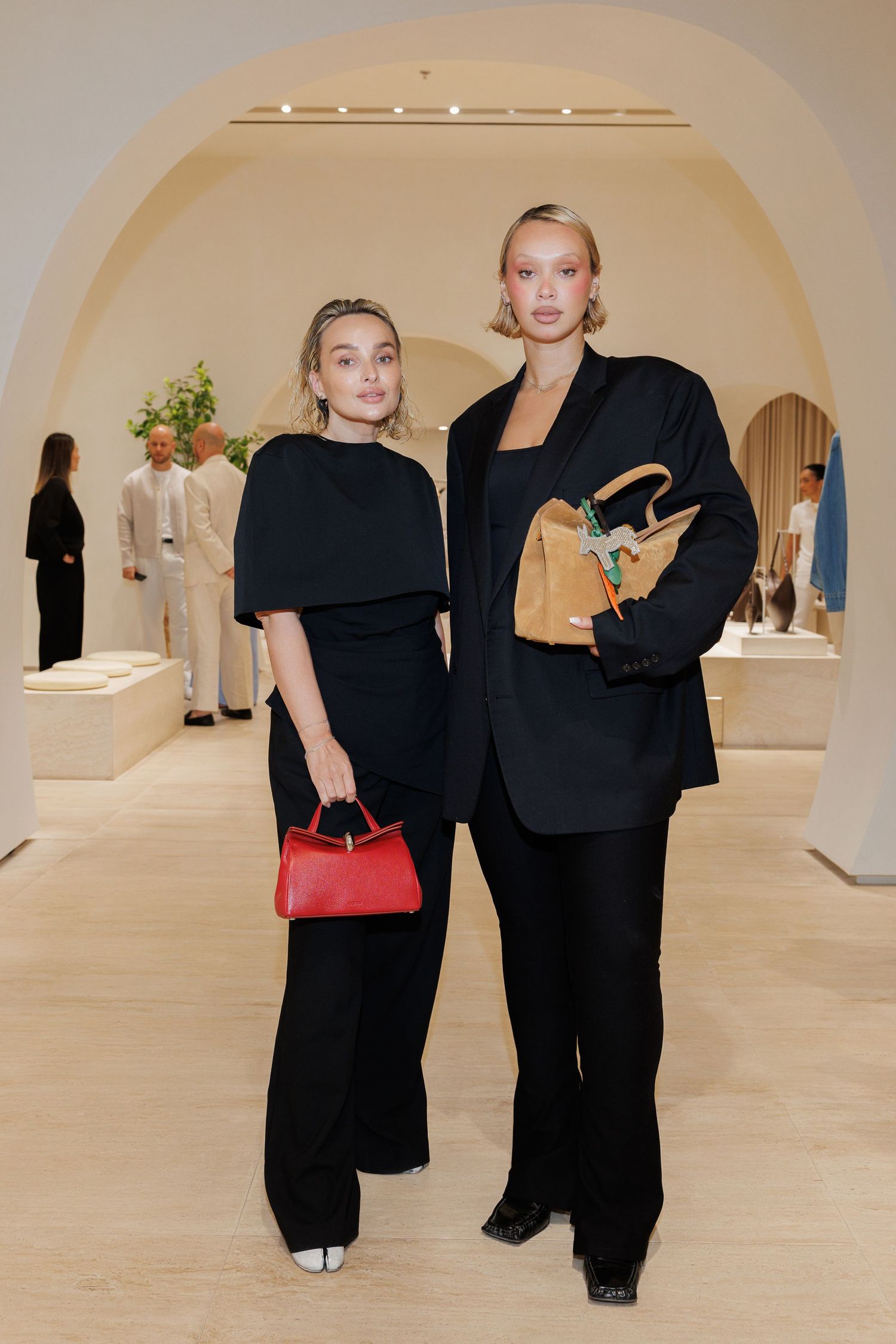 People in black outfits standing in a minimalist gallery space with arched ceilings.