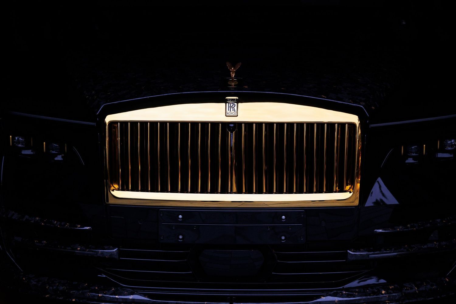 Illuminated Rolls-Royce Spirit of Ecstasy hood ornament glowing in darkness.