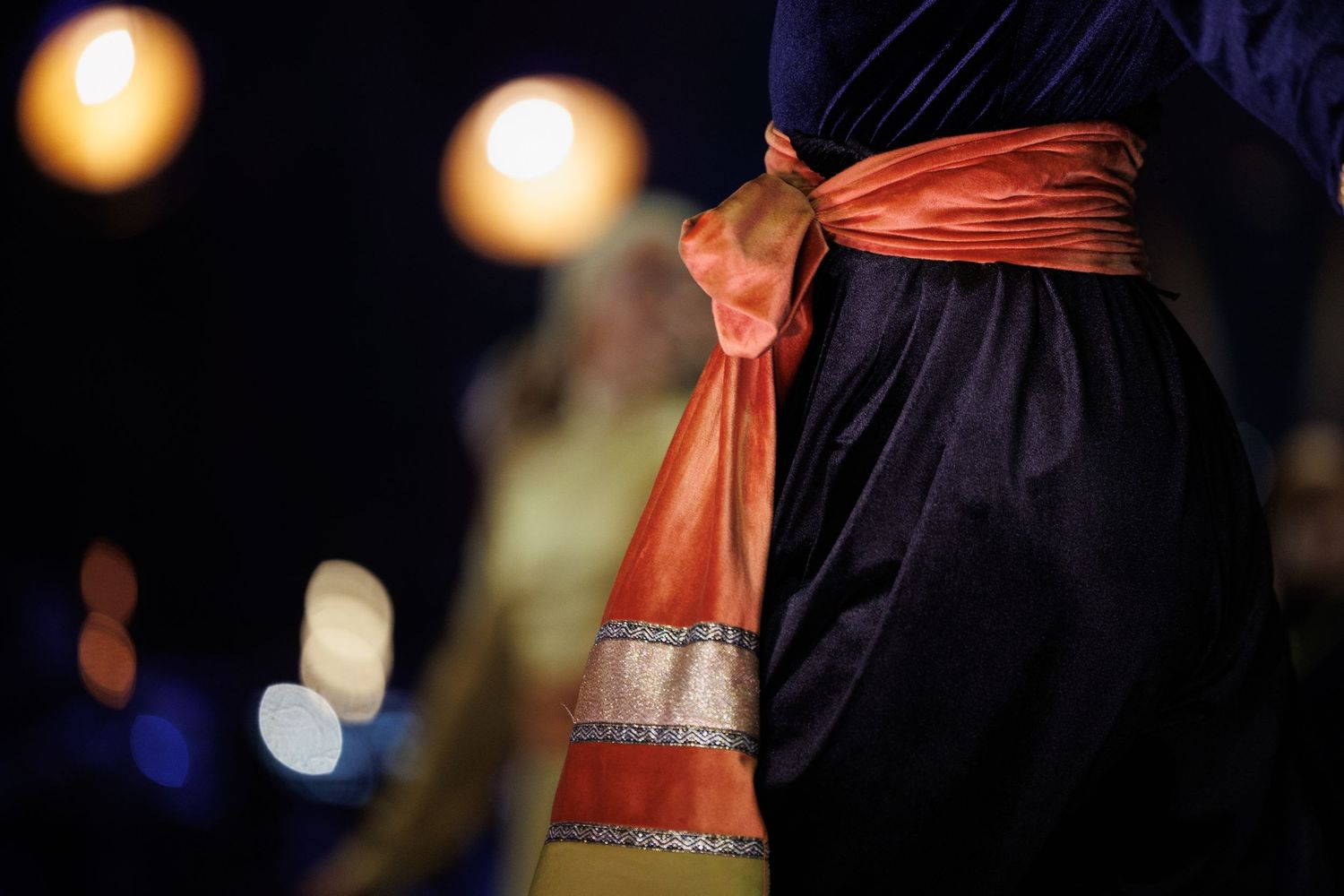 Close-up of an ornate red and gold sash detail on a navy blue performance costume.