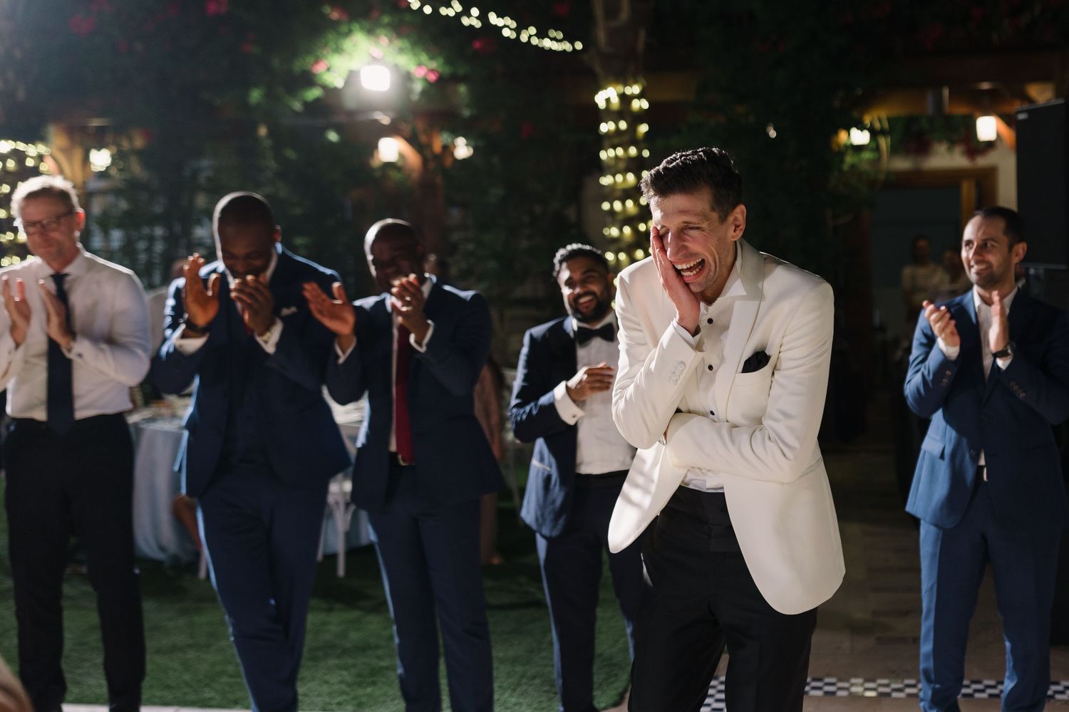 Groomsmen in suits watching and reacting during wedding reception.