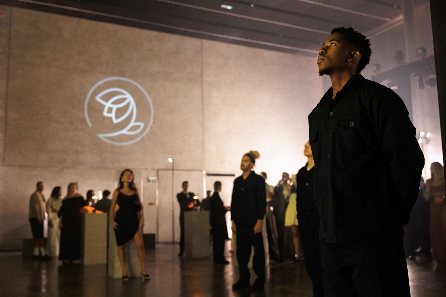 Dark gallery space with silhouettes of visitors and illuminated circular logo on wall.