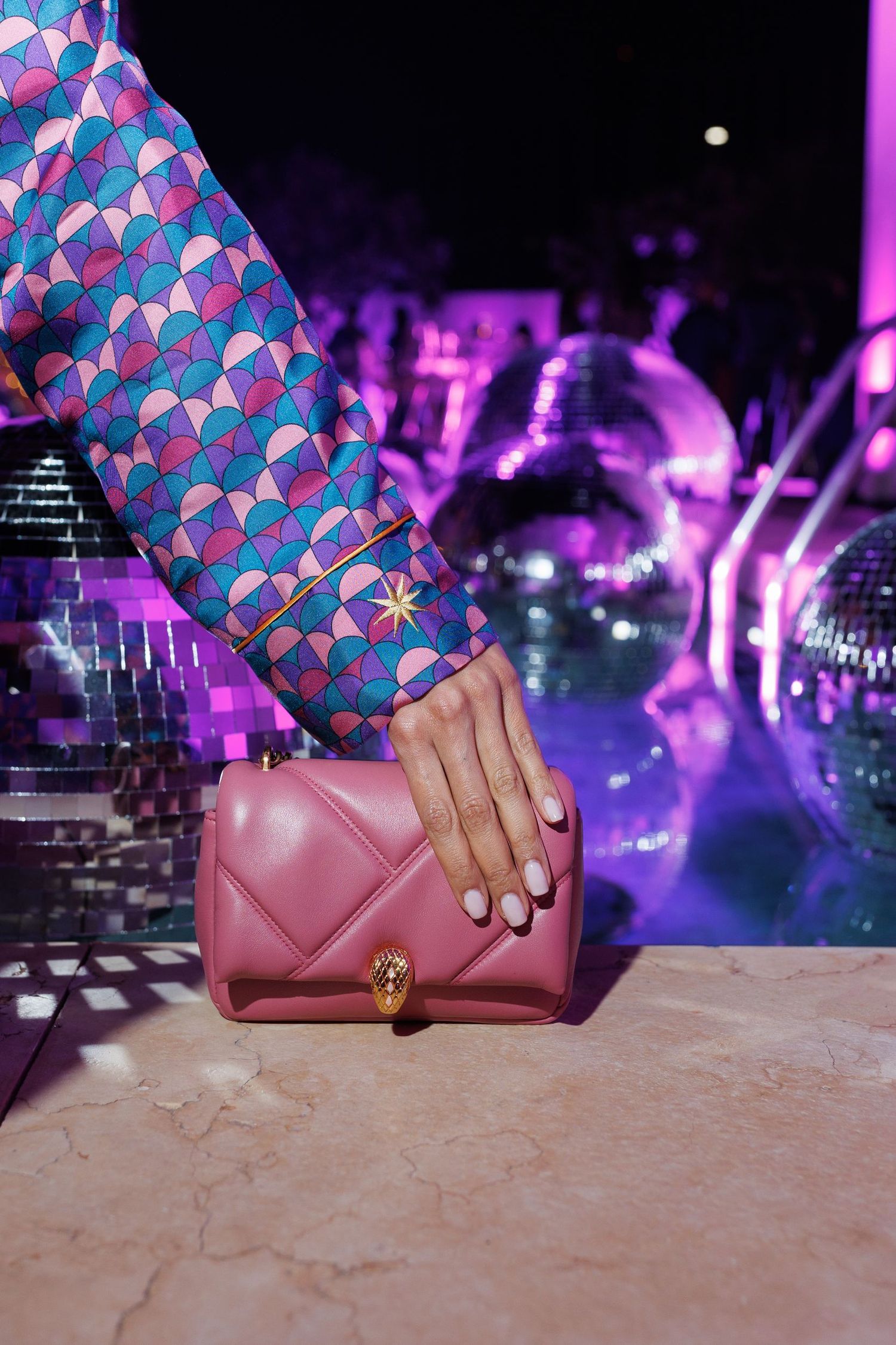 Pink leather wallet displayed against purple-lit party background.