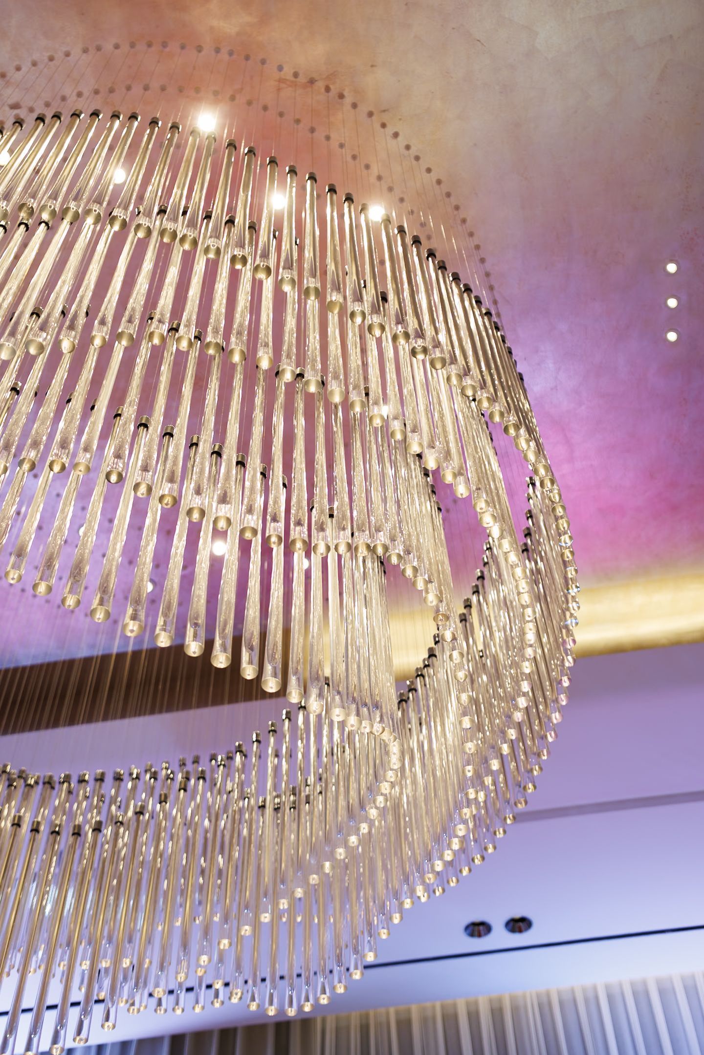 Luxurious spiral crystal chandelier with modern design illuminated in purple ambient lighting.