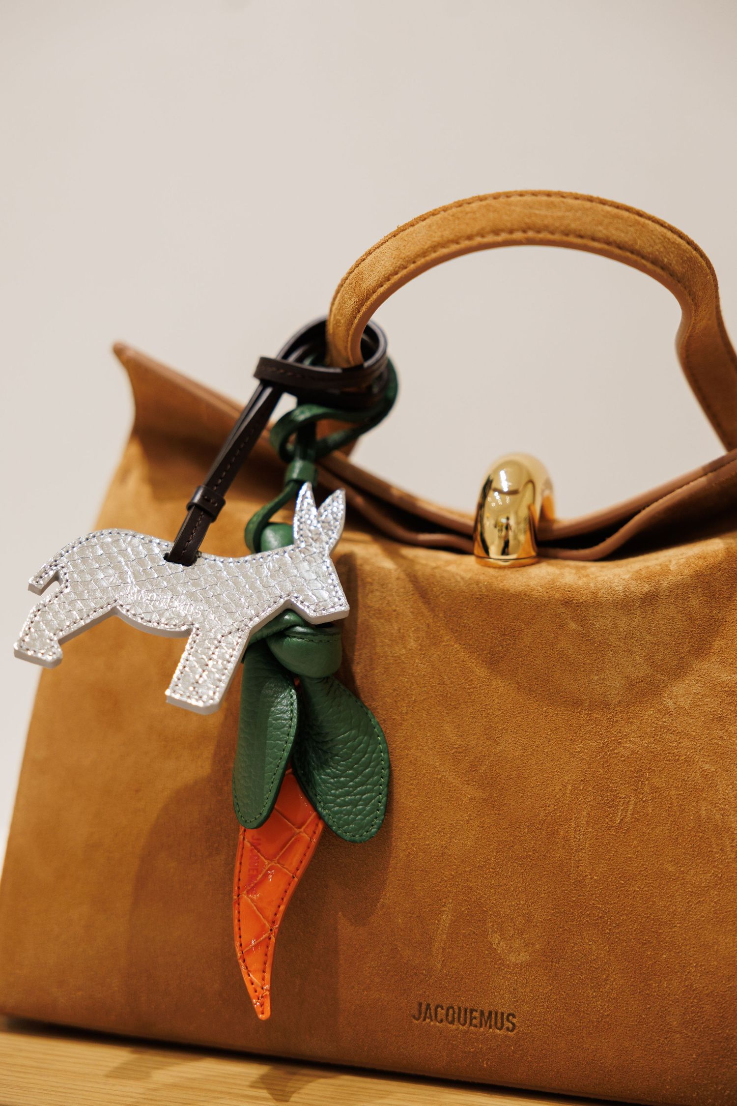 Tan suede Jacquemus handbag with decorative crystal unicorn and leather charms.