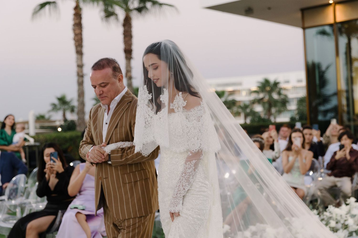 Elegant outdoor wedding ceremony setup with white floral arrangements and palm trees.