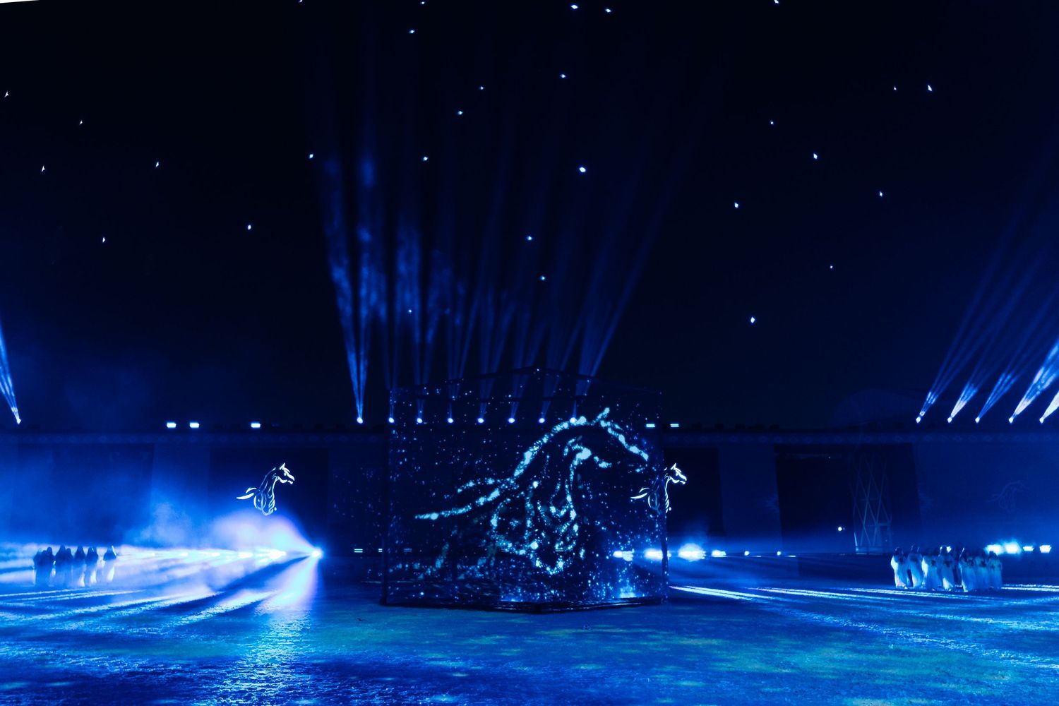 A dramatic stage performance with blue spotlights illuminating a large dinosaur skeleton silhouette against a starry backdrop.
