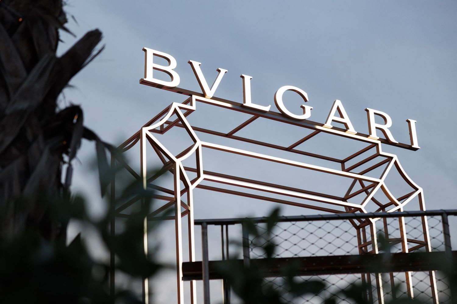 Illuminated Bvlgari logo signage displayed against a twilight sky.