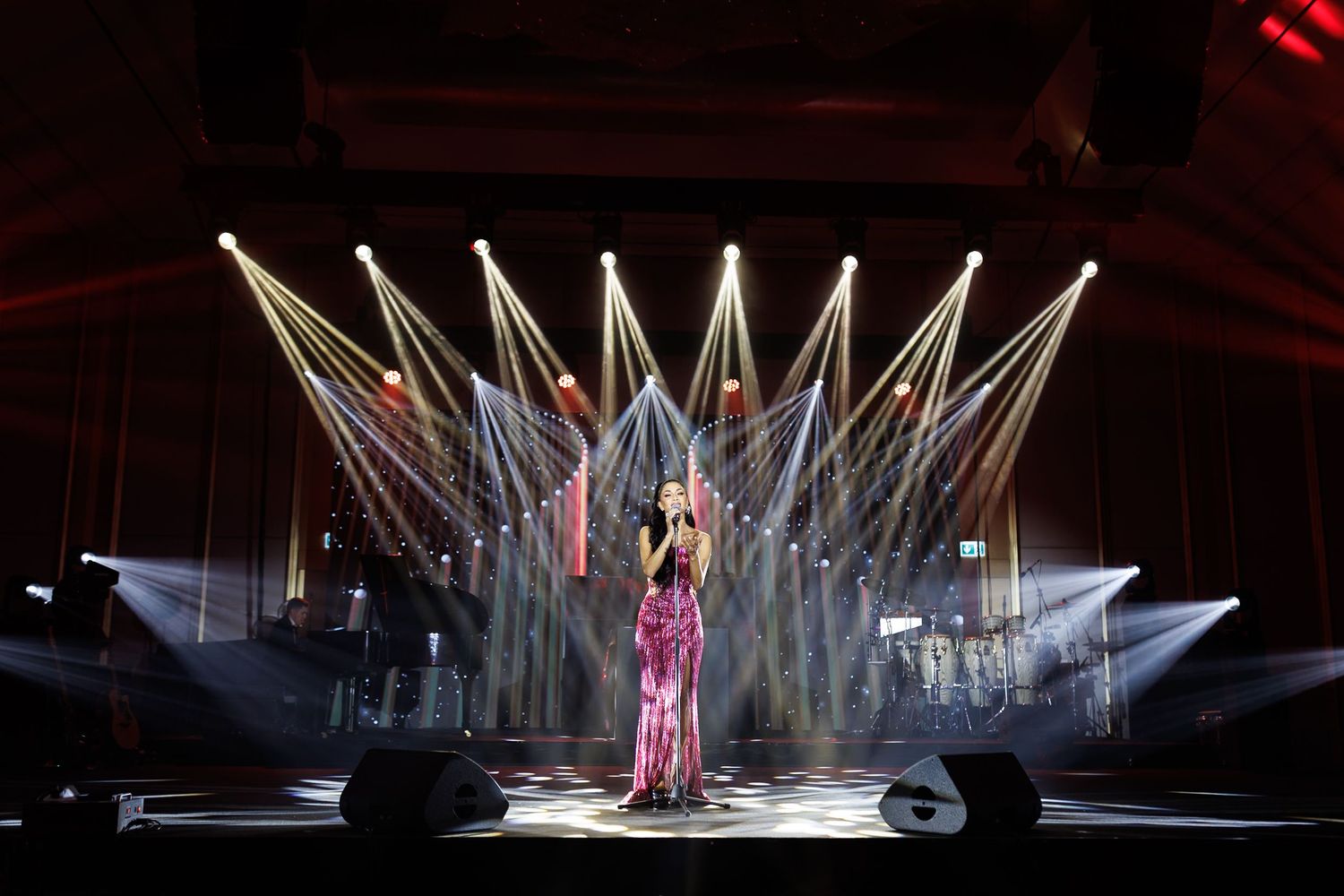 Dramatic spotlights create a fan pattern of white beams around a performer on stage.