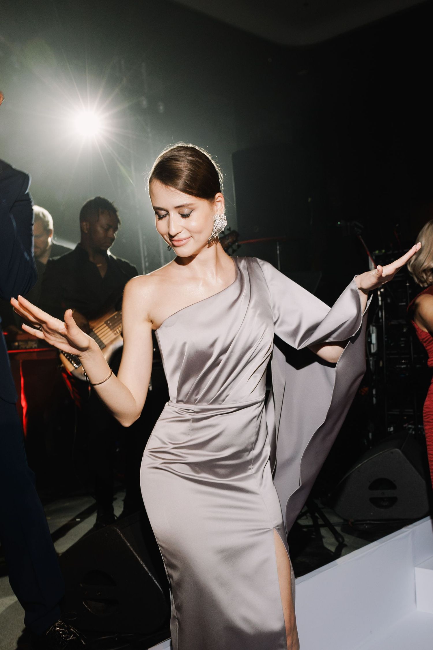 Dancing figure in a flowing silver dress under dramatic spotlight at an event.