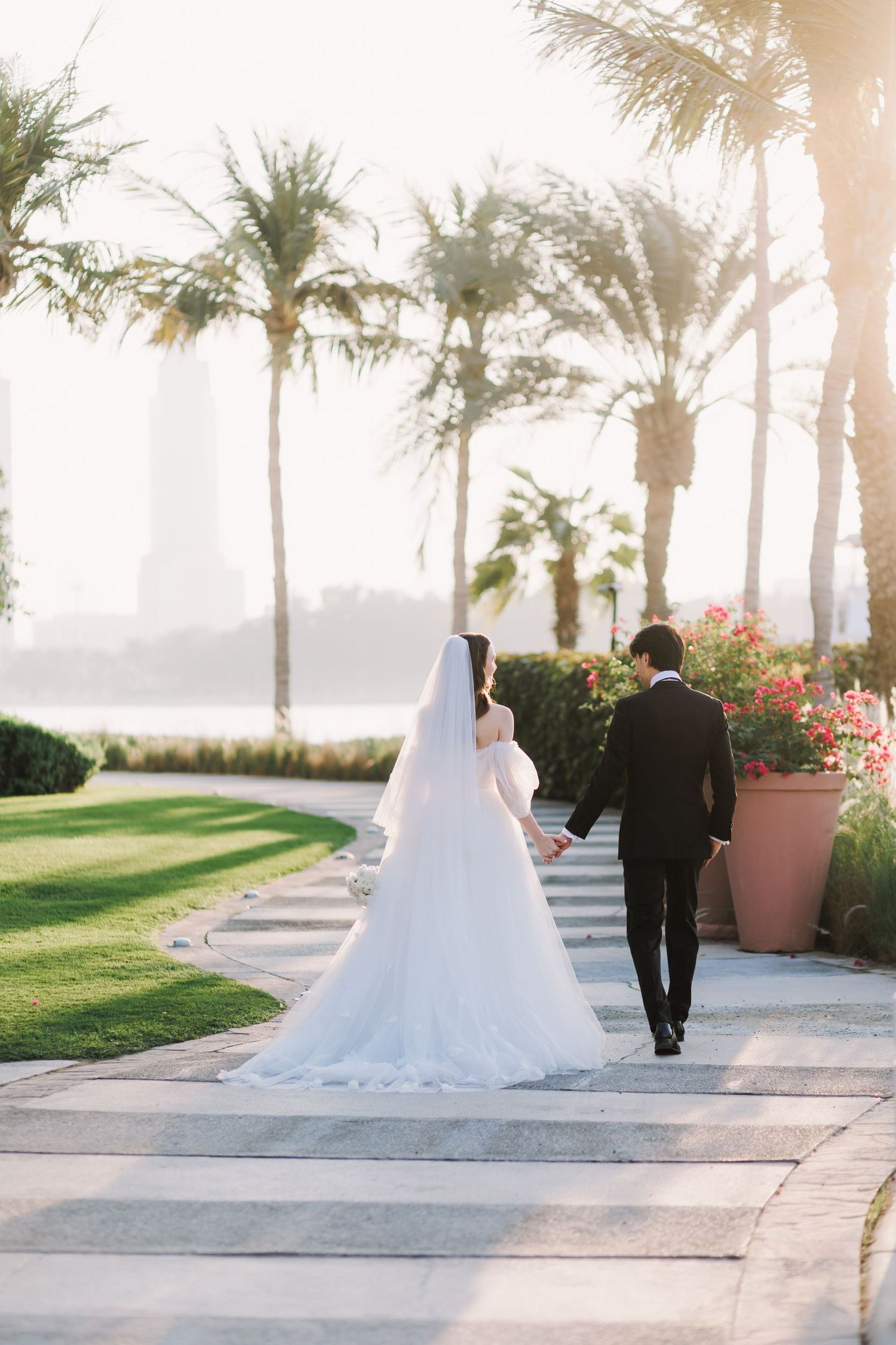 Wedding couple walking along palm-lined path at sunset.