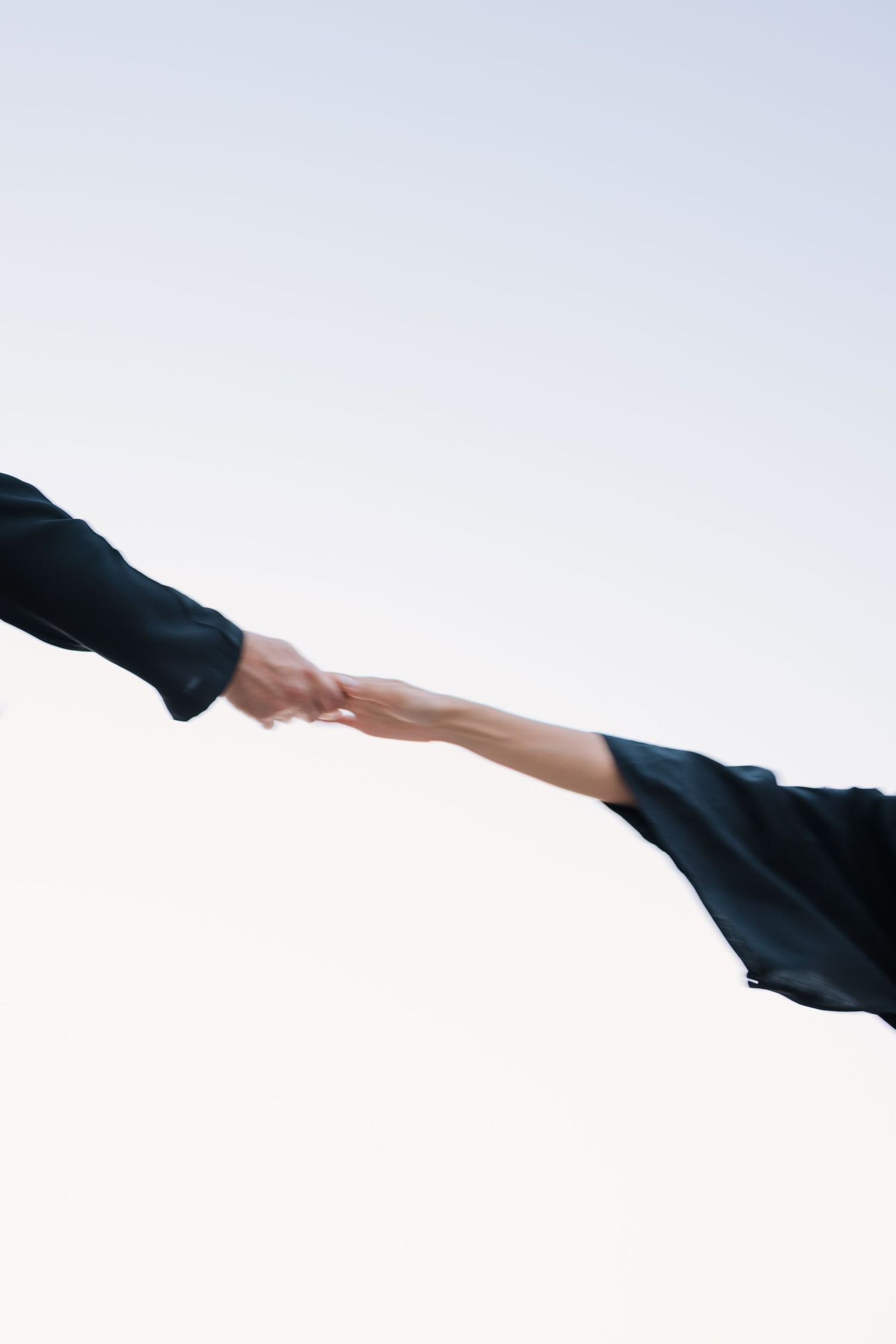 Minimalist composition of reaching hands against white background with black sleeves.